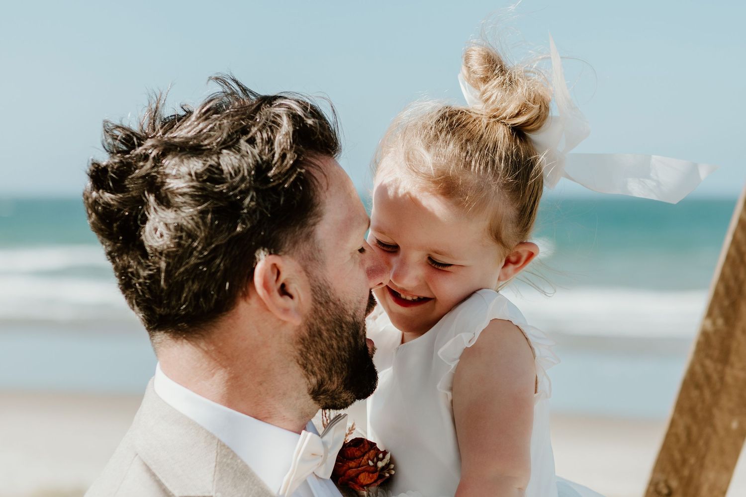 A tender moment of laughter and joy shared between two people against a sunny beachside backdrop.