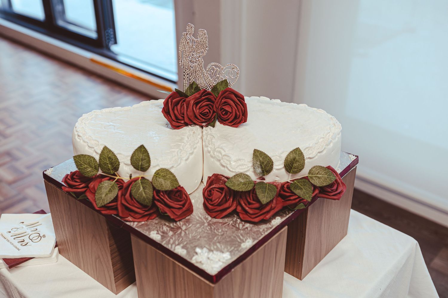 Three decorative red and cream-colored paper flowers arranged on a light wooden surface with white lace accents.