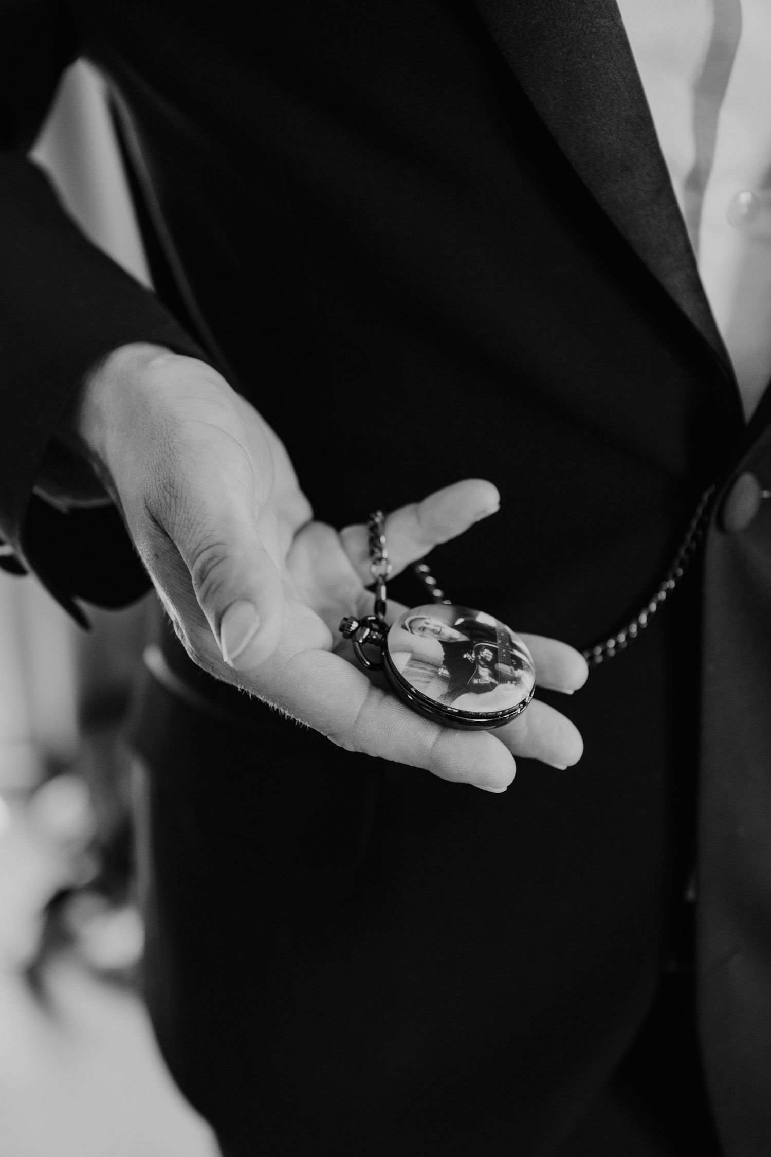 A hand in formal attire holds an antique pocket watch with dark shadows and highlights in black and white.