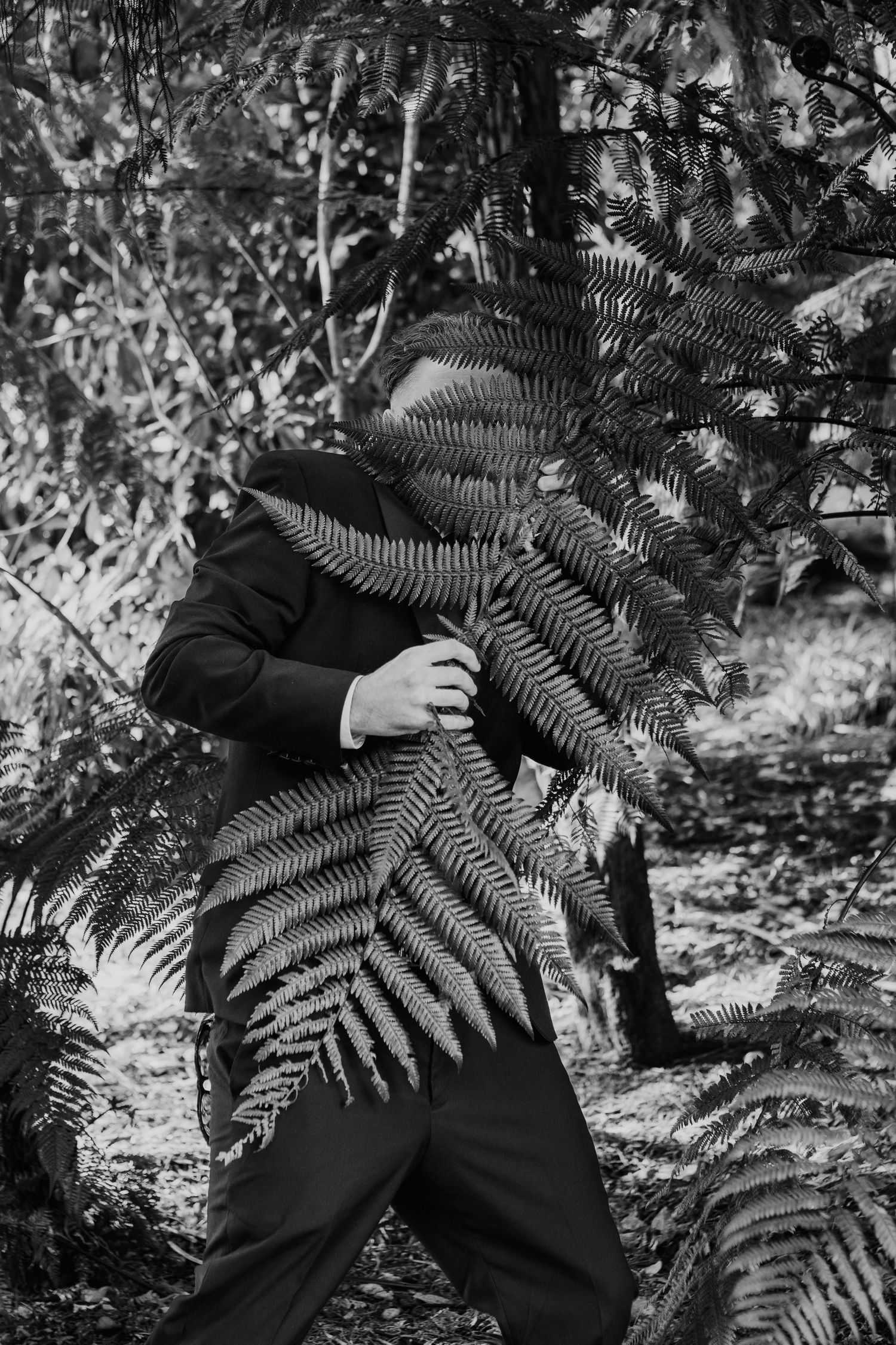 Black and white artistic photographs show a person lying among large fern leaves in a garden setting.
