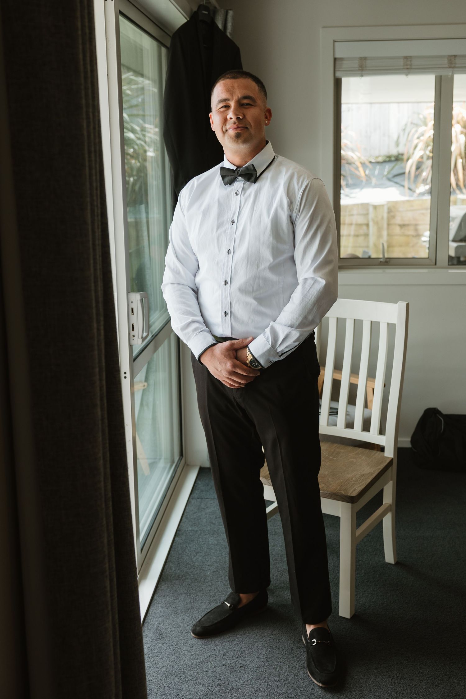 A person in formal attire stands on a porch with white railing and gray carpeting in natural lighting.