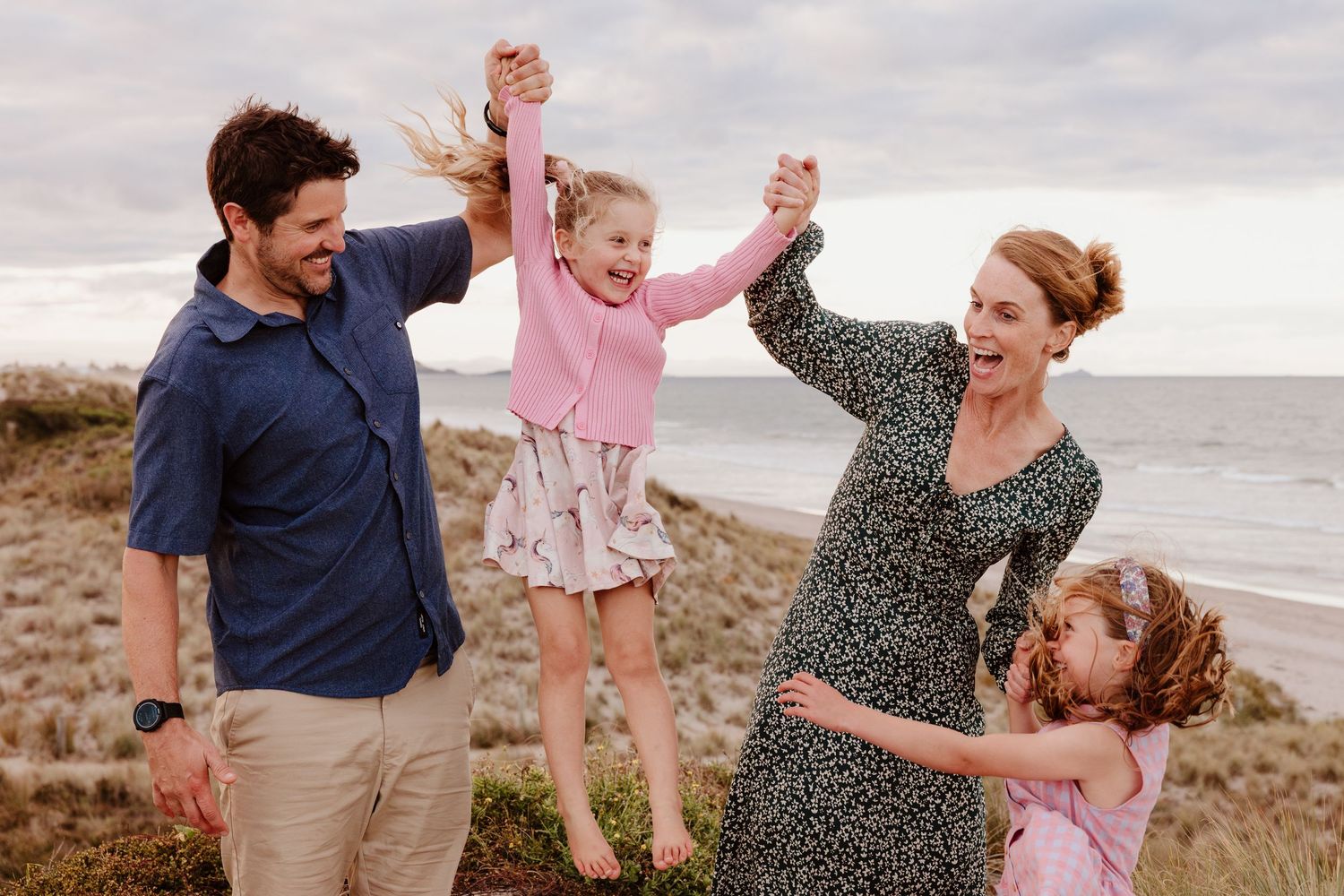 A family plays and dances together on a sandy beach at sunset creating joyful moments by the ocean.