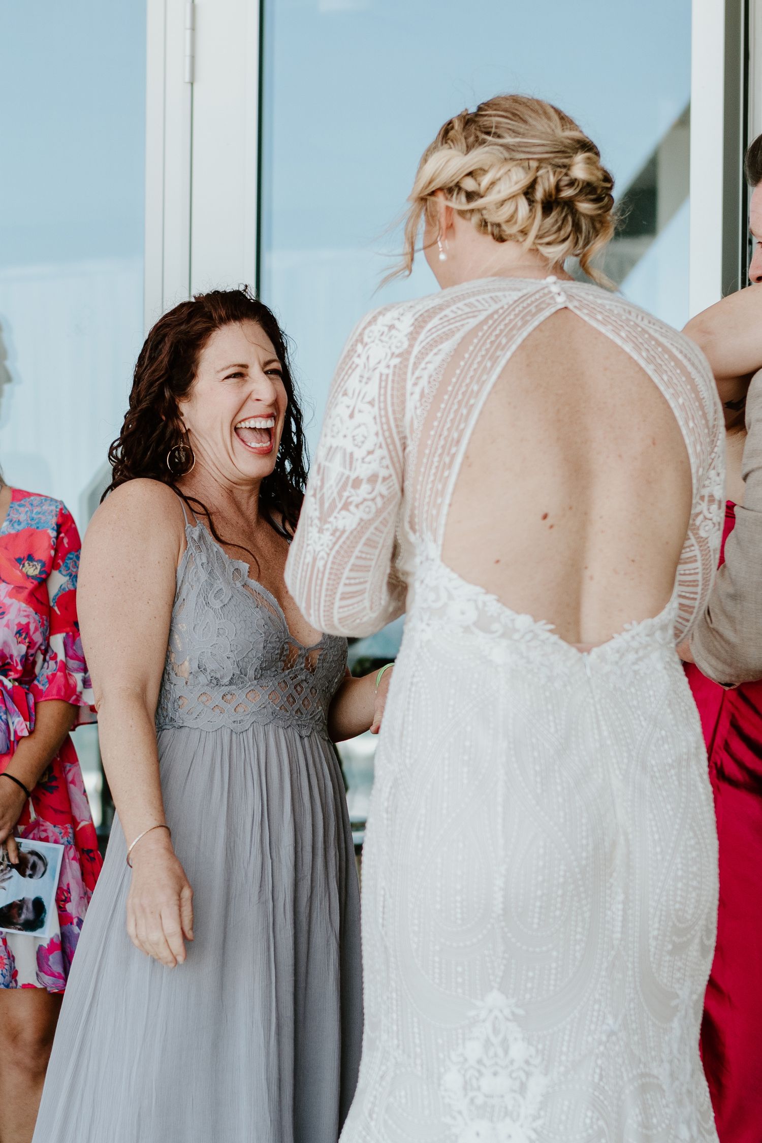 Bridesmaids in gray dresses sharing laughter during wedding preparations. Papamoa Surf Lifesaving Club Wedding