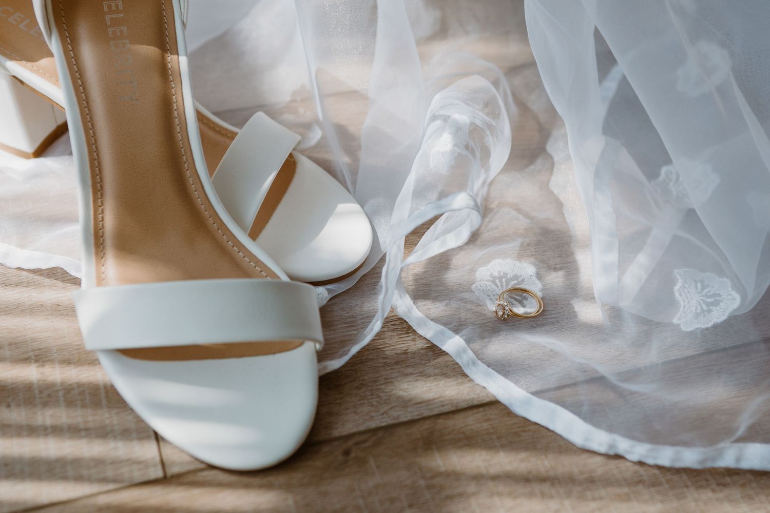 Elegant white wedding shoes and veil arranged on light fabric with ring detail.
