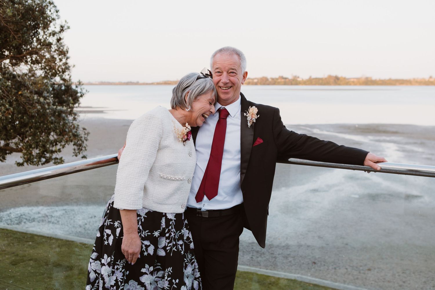 Happy couple embracing and laughing together during sunset by the water's edge.