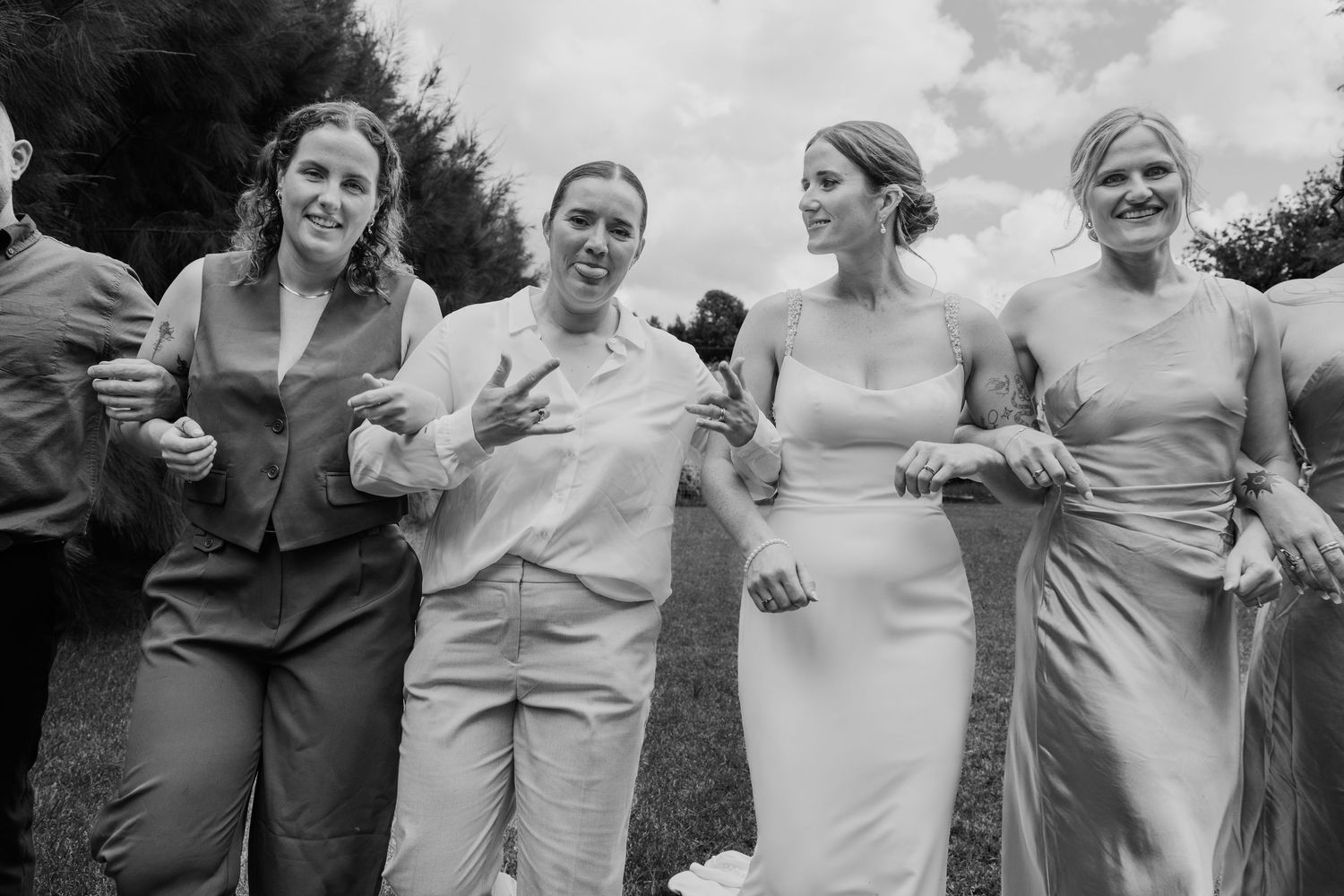 Black and white photo of bride and bridesmaids laughing and walking together outdoors at a wedding celebration.