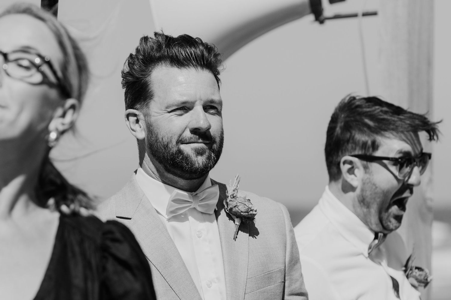 A candid black and white photo shows grooms reaction during a wedding ceremony. Papamoa Surf Lifesaving Club Wedding