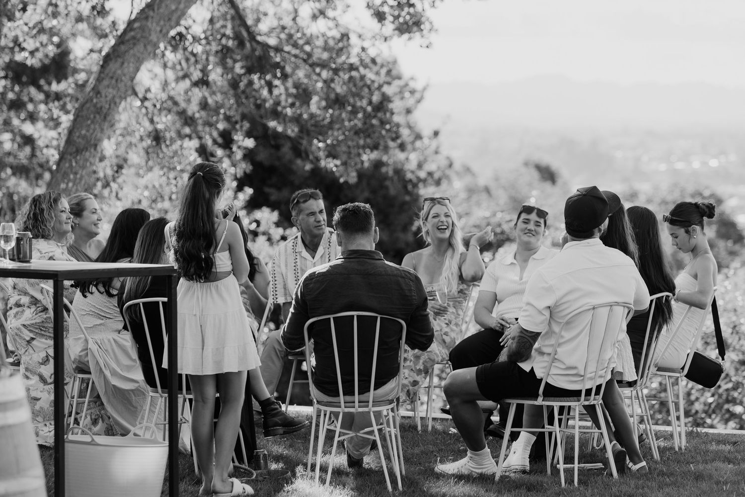 Black and white photo of a group of people sitting in chairs outdoors at a garden gathering or wedding reception.