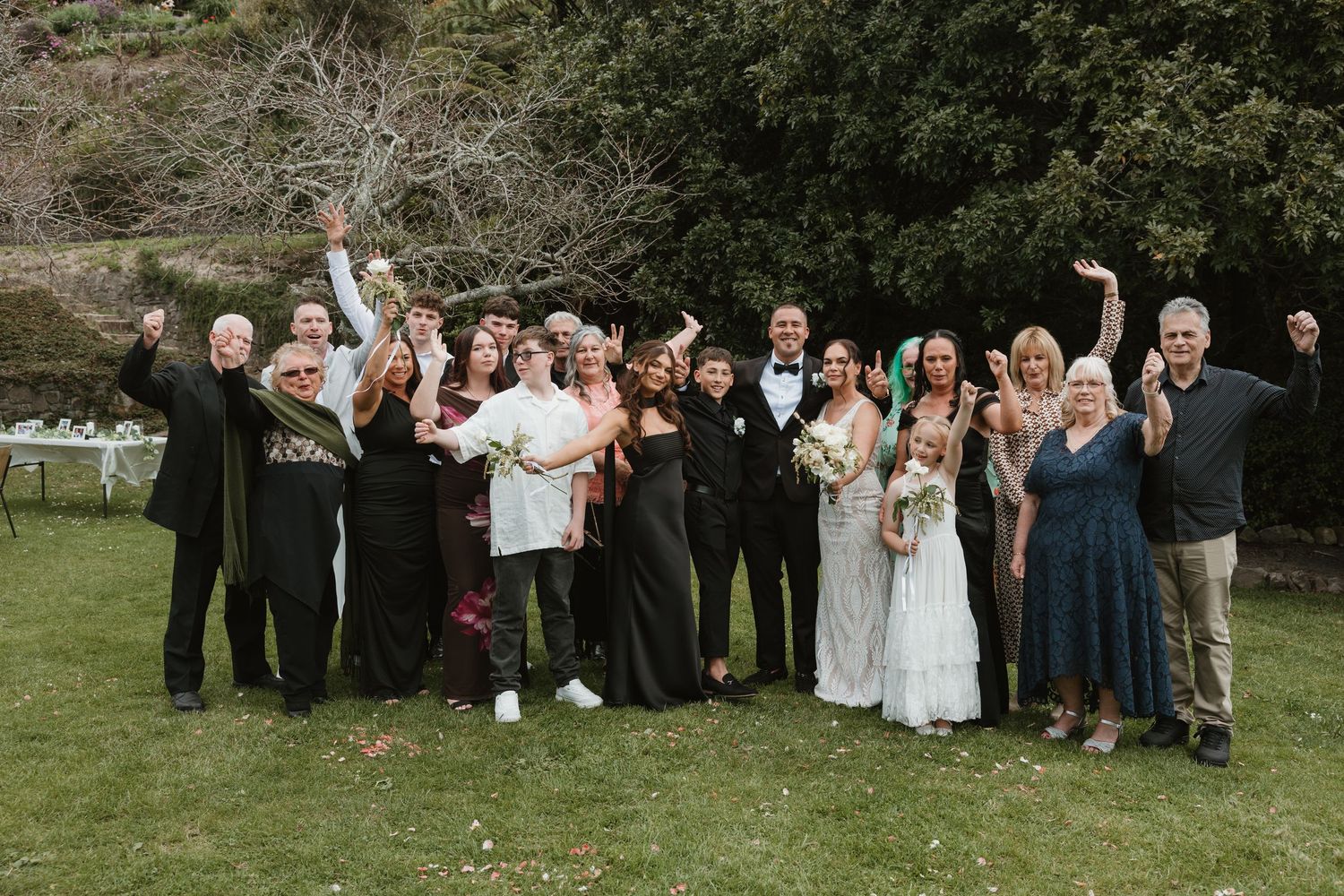 Wedding party and guests gather on a grassy lawn for group photos at an outdoor celebration.