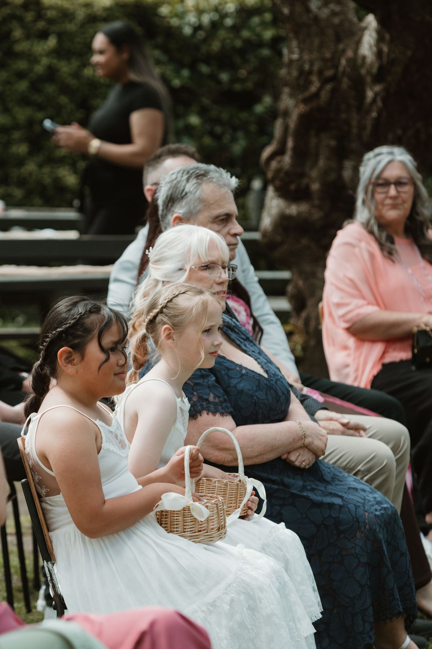 Guests seated outdoors at a wedding ceremony watching the proceedings with attentive expressions.
