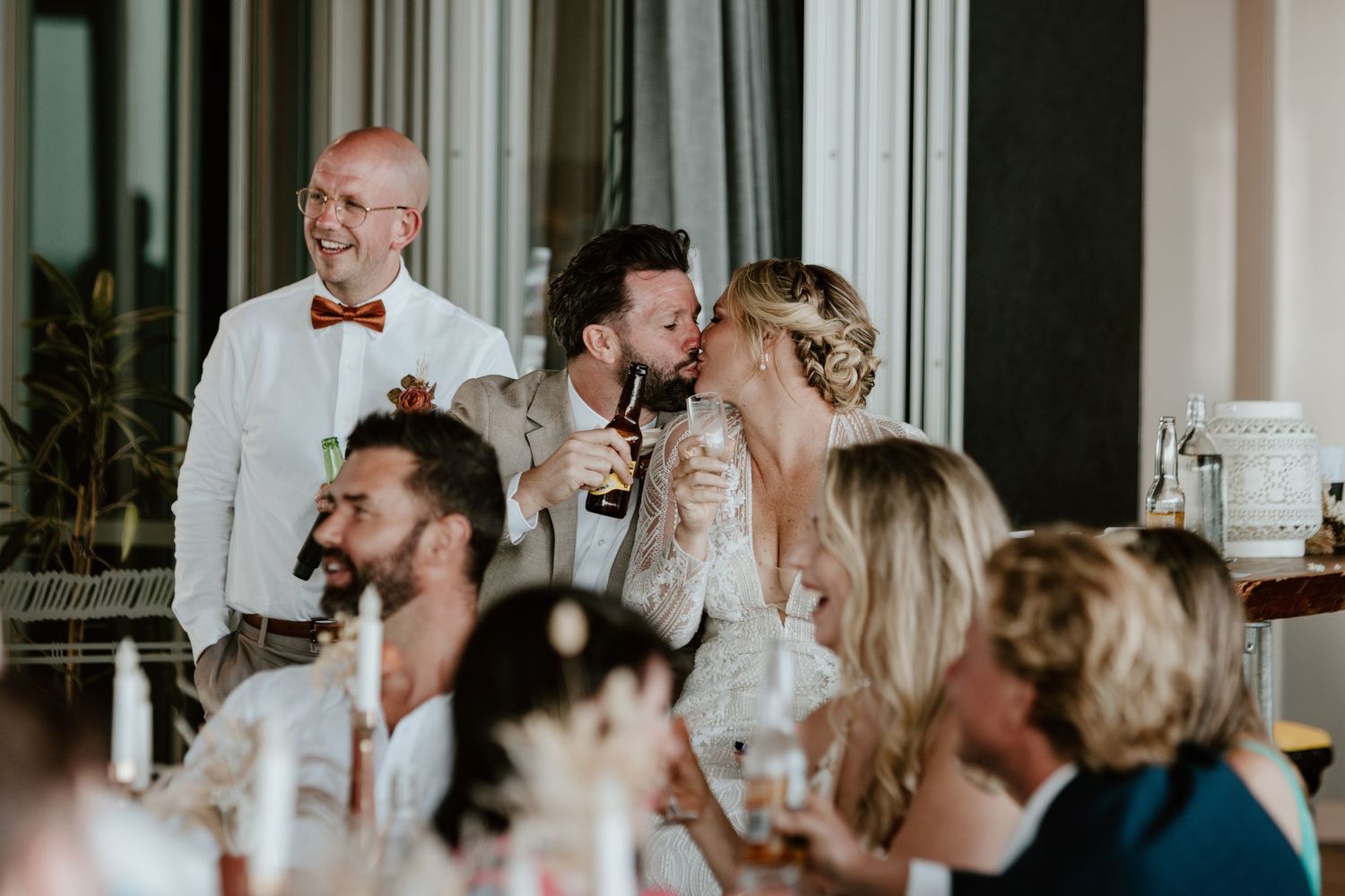 Wedding guests laugh together during reception speeches at an evening celebration.