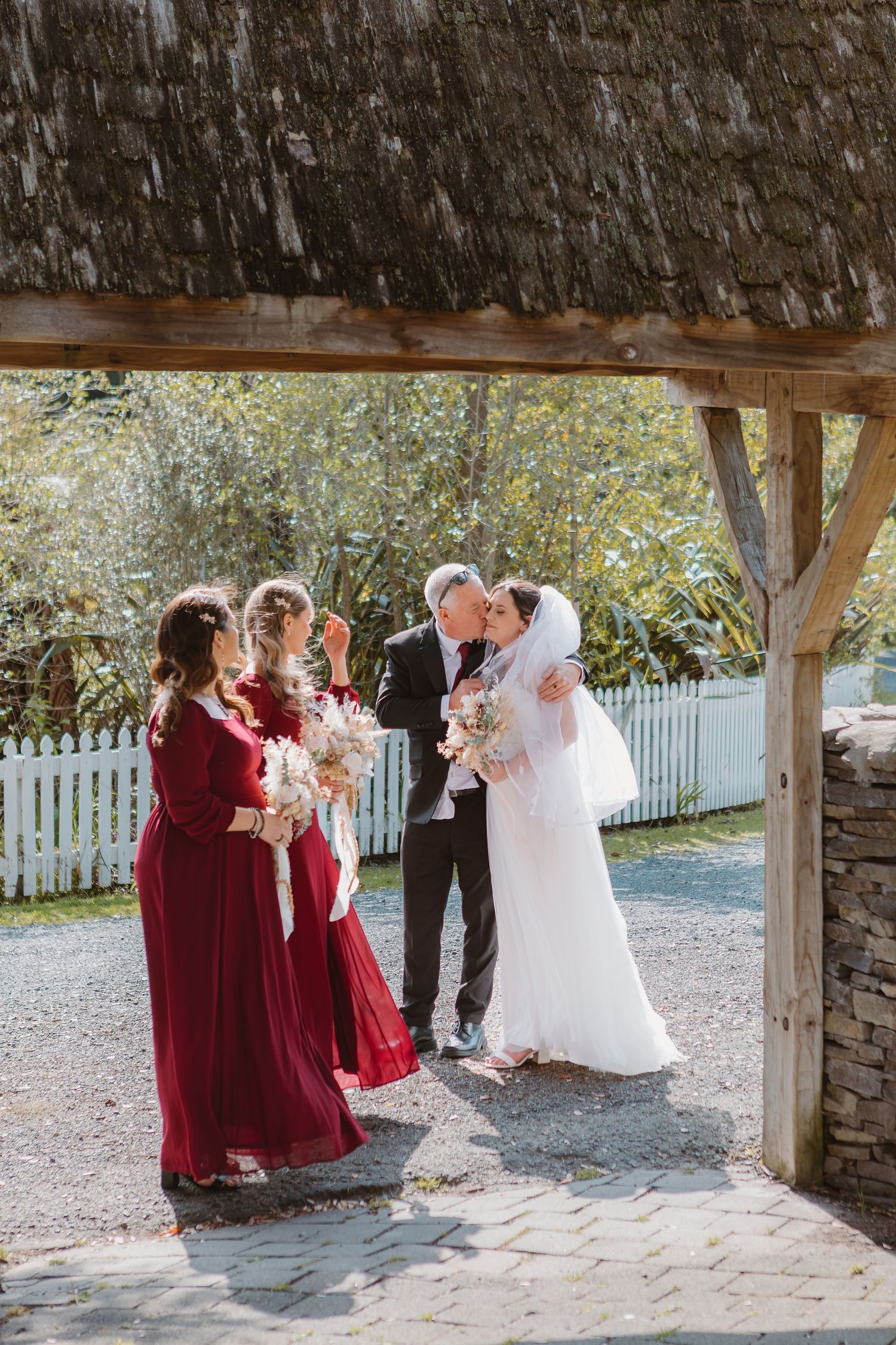 Wedding party celebrates under a rustic wooden pavilion with beautiful fall foliage in the background.