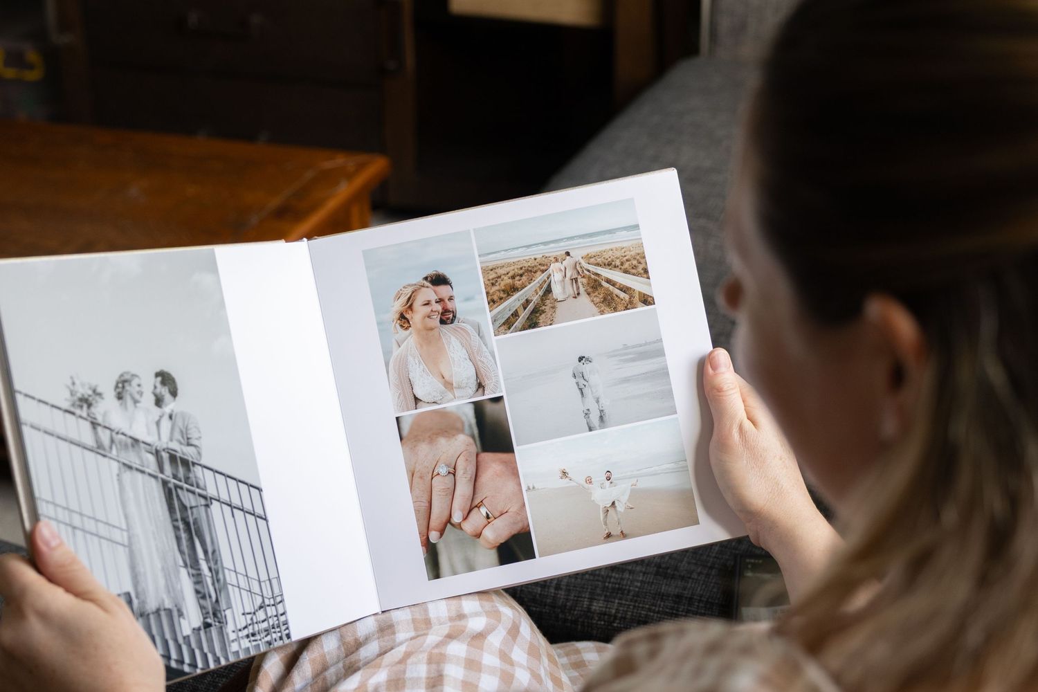 Someone flips through a wedding photo album showing professional photographs from a coastal ceremony.