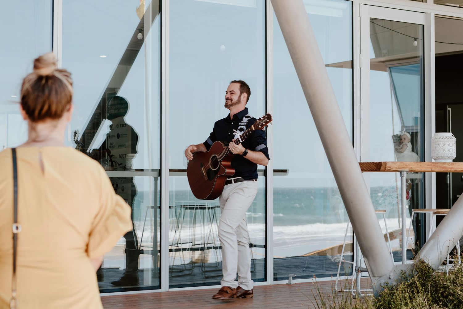 Live musician performs with acoustic guitar on a beachfront venue patio. Papamoa Surf Lifesaving Club Wedding
