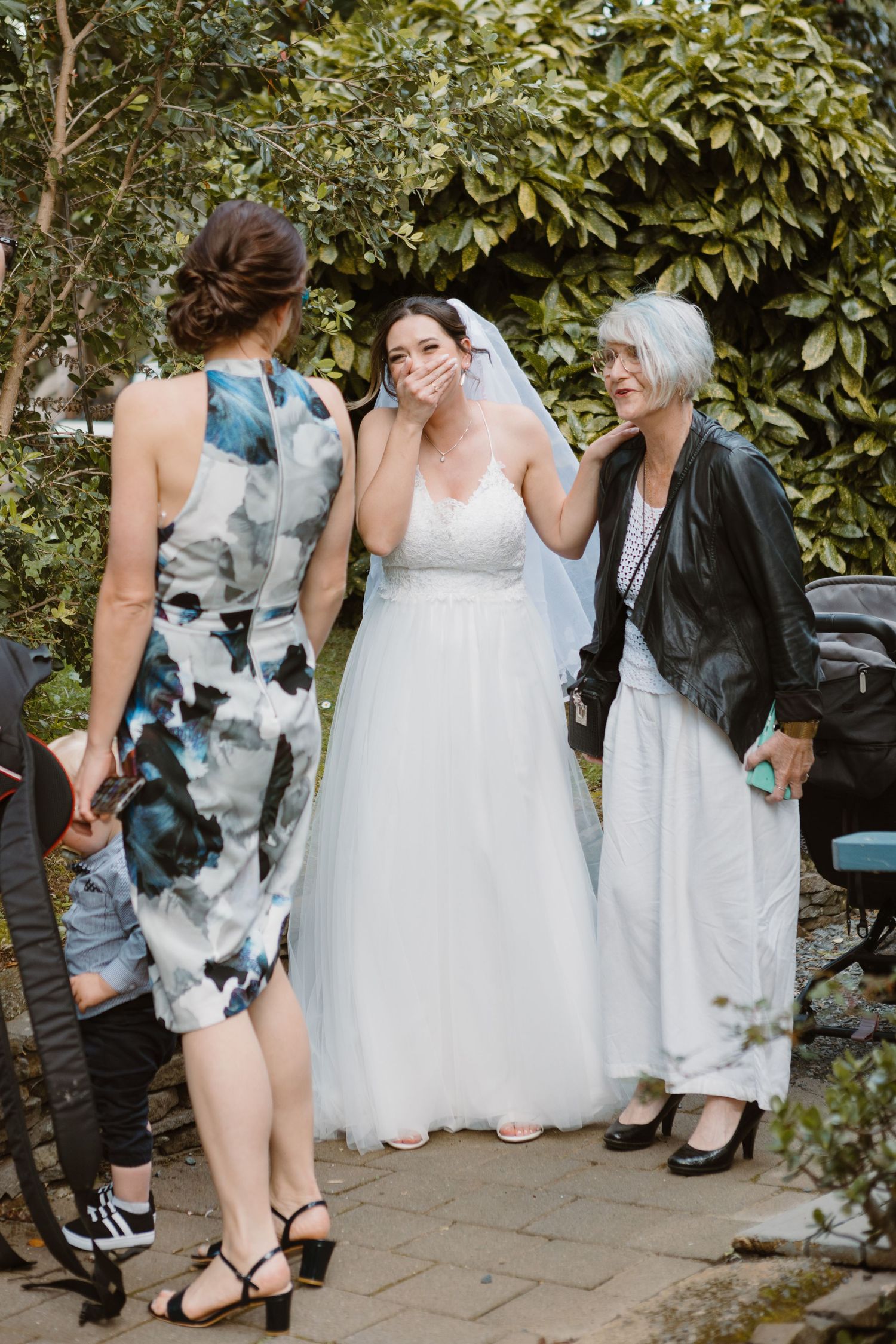 A bride in a classic white wedding dress shares a moment with guests in an outdoor garden setting.