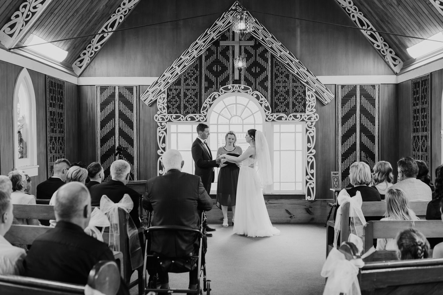 Wedding guests observe a ceremony in a charming chapel with intricate geometric patterns and white trim.