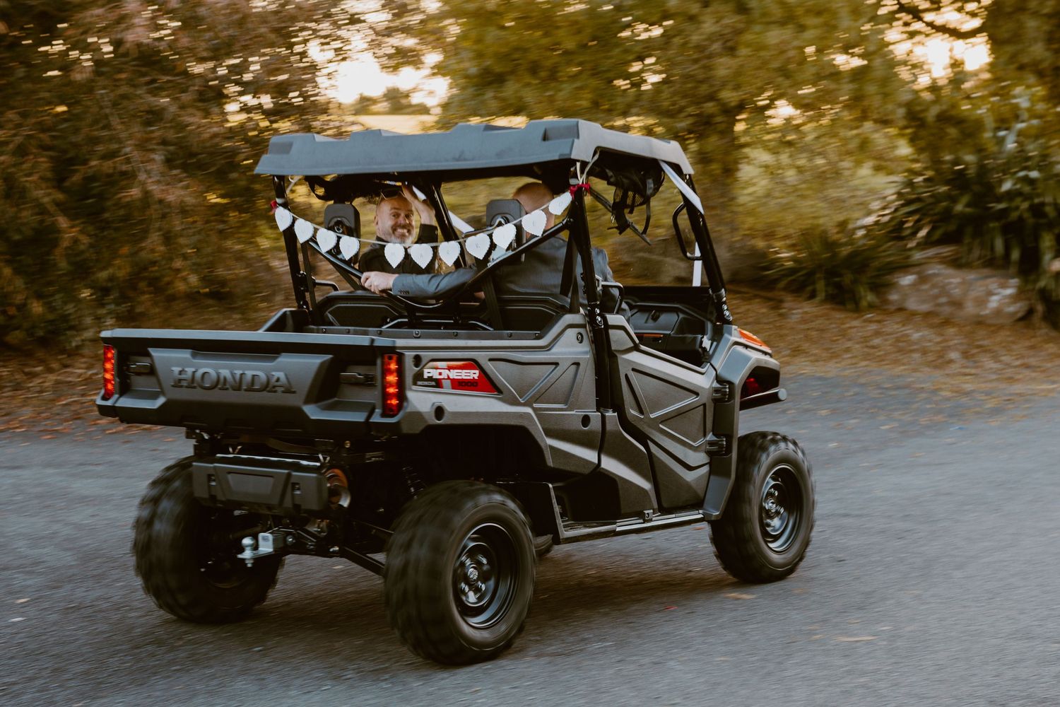 All-terrain utility vehicle decorated with paper jack-o'-lantern decorations driving on a dirt path at sunset.