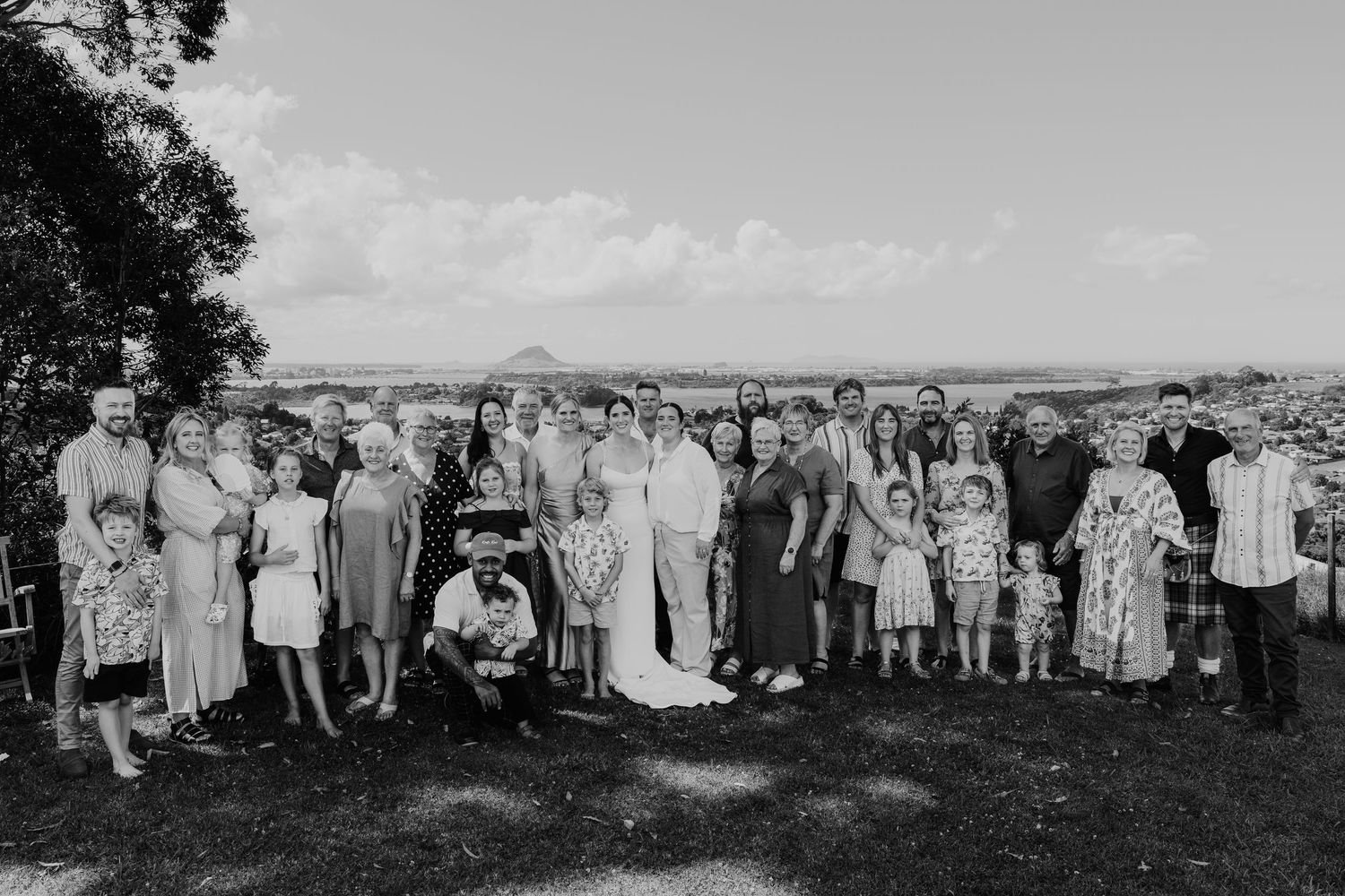 Black and white wedding group photo with bride, groom, and family outdoors with scenic mountain backdrop.