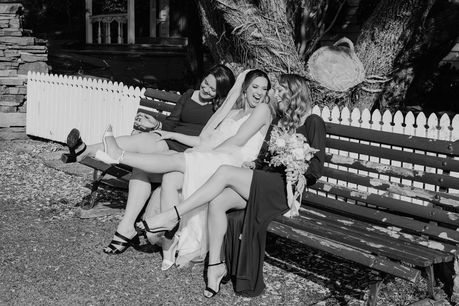 Wedding party members relax on a garden bench during an outdoor photo session.
