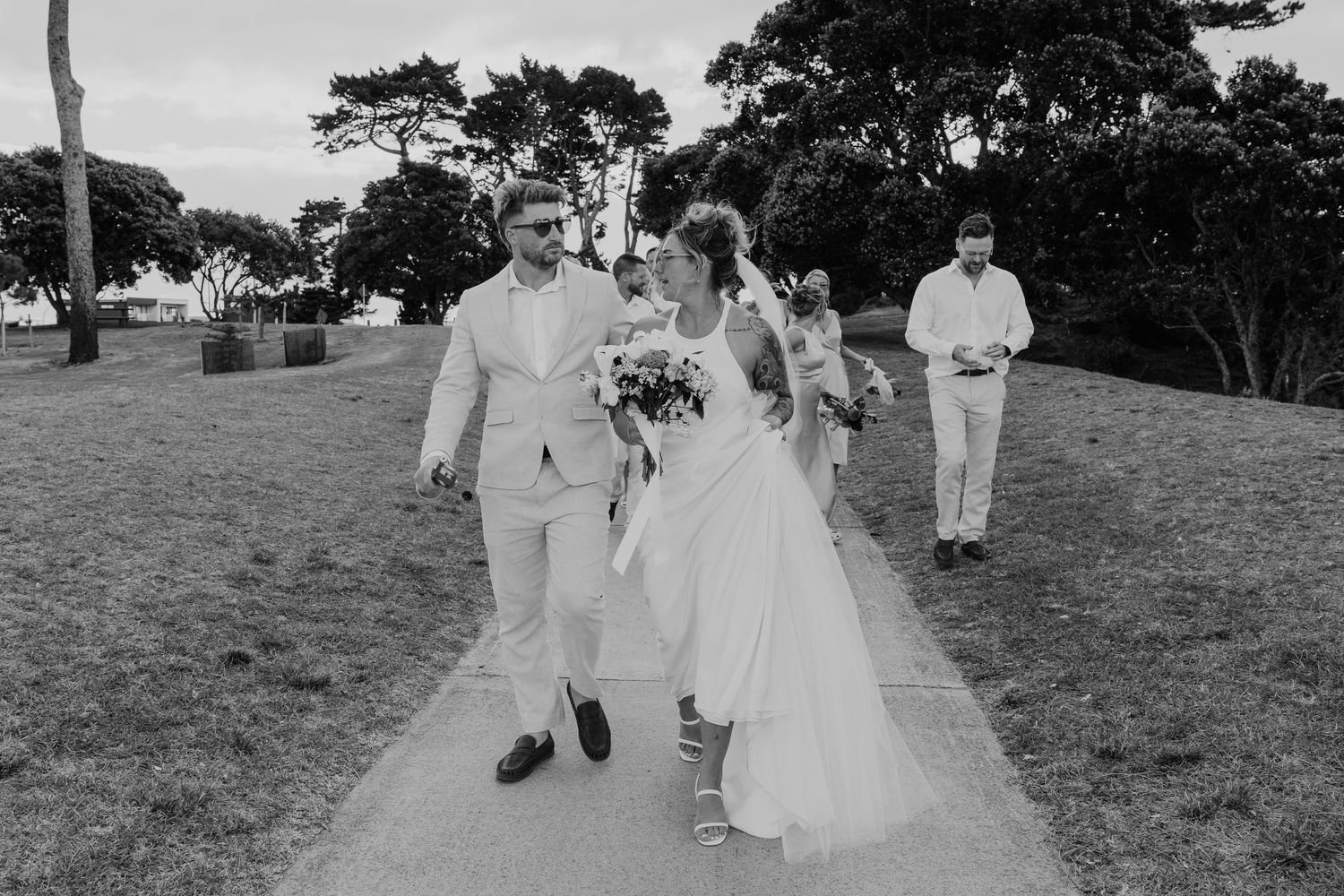 Black and white photo of a bride and groom walking down a path at an outdoor wedding ceremony.