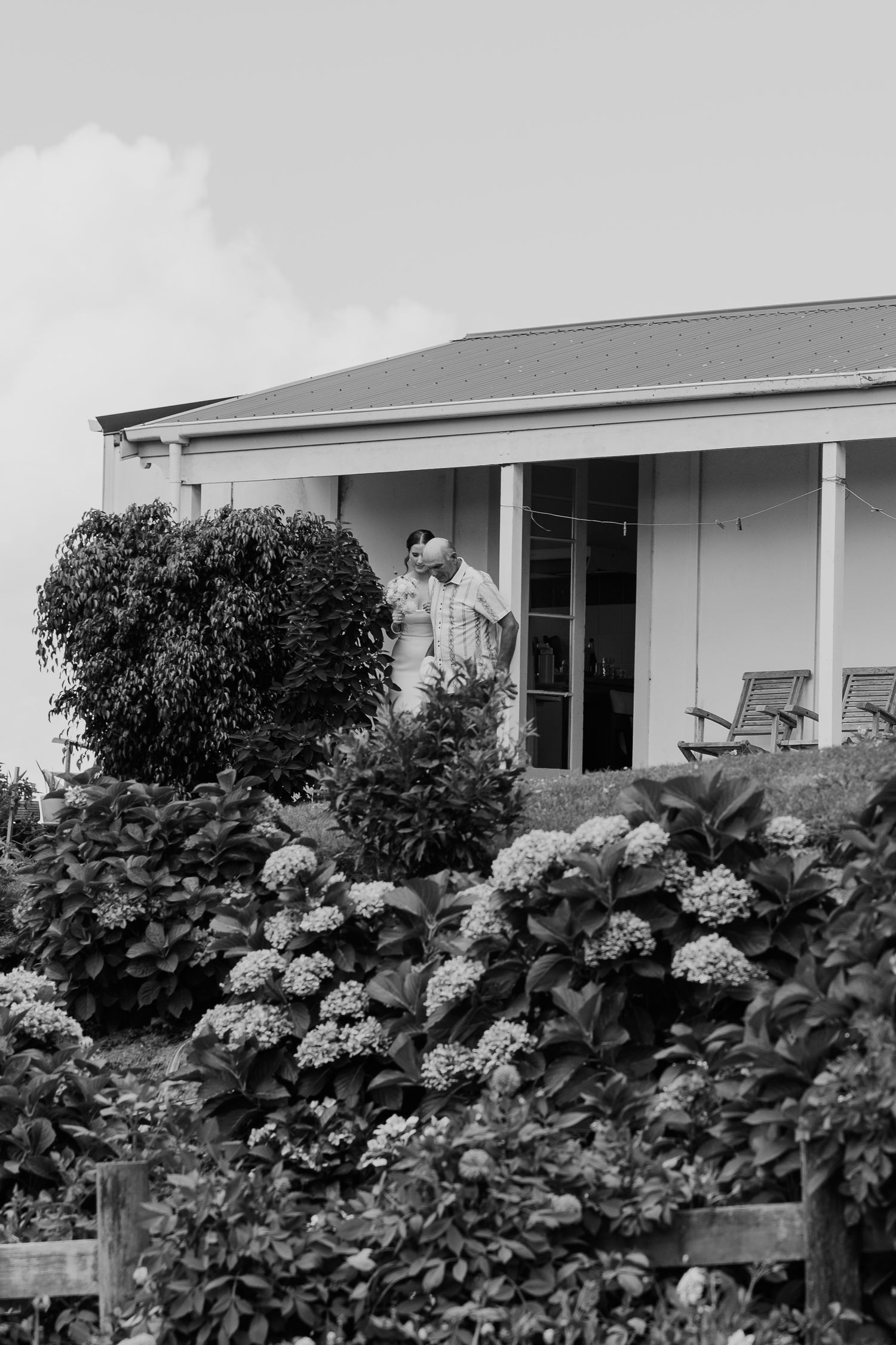 Couple sharing a kiss on a porch surrounded by blooming hydrangeas and lush greenery in black and white.
