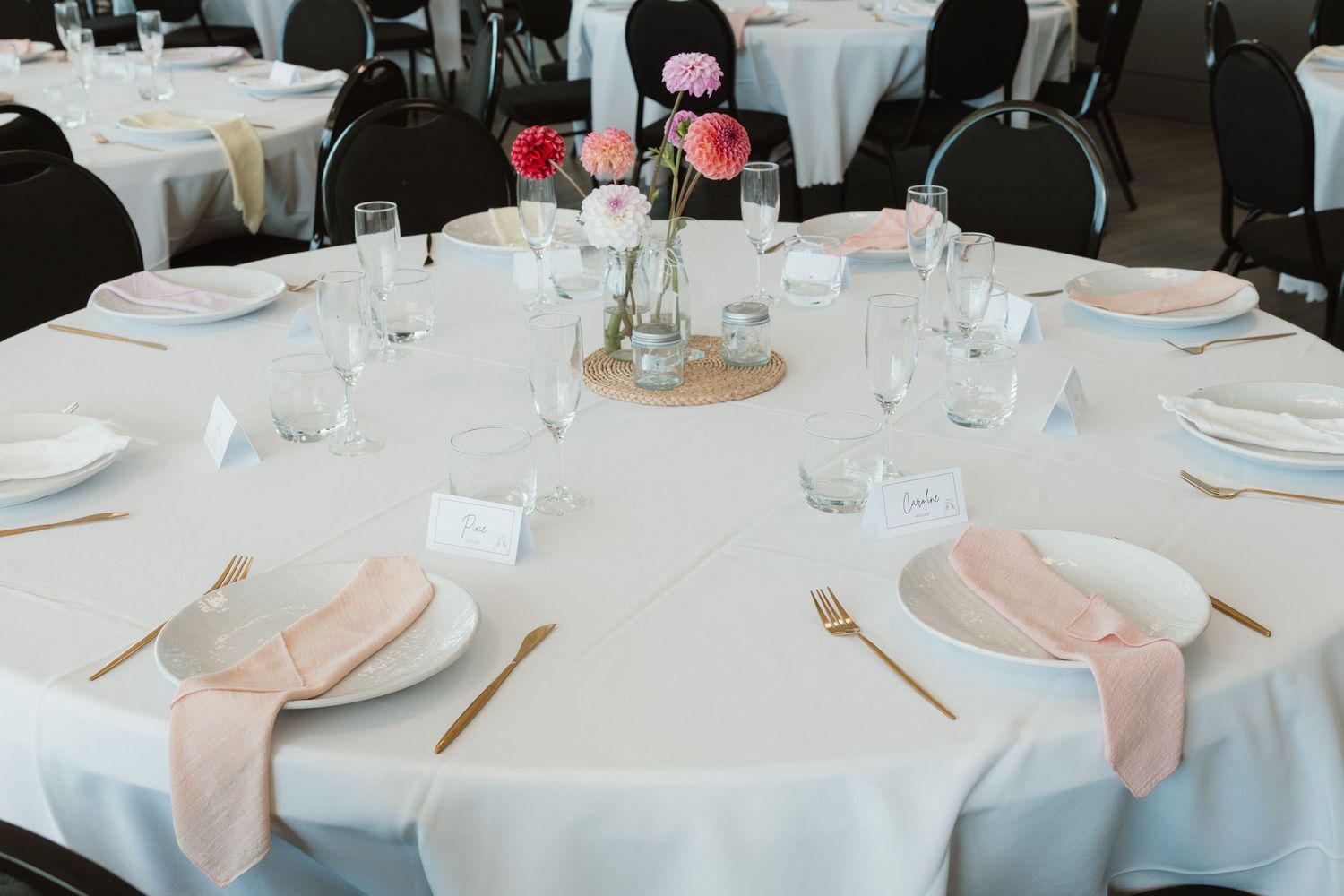 Elegant wedding reception table set with white linens, pink napkins, gold cutlery, and floral centerpieces.