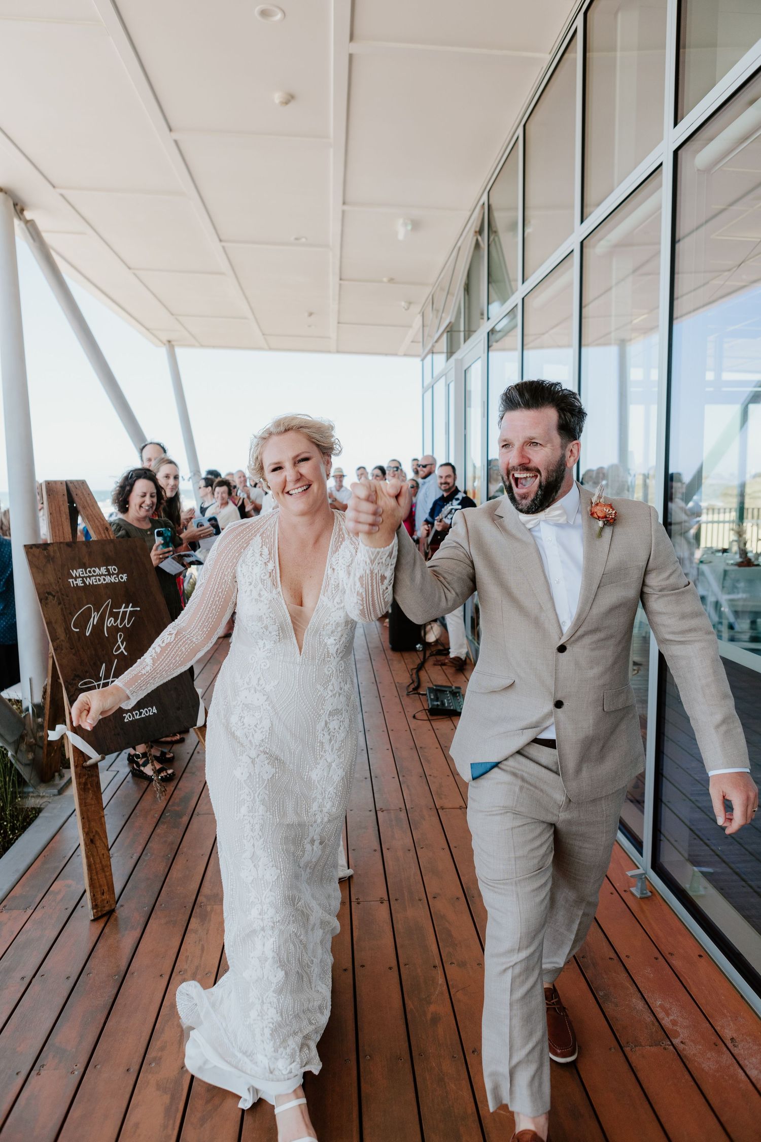 A joyous couple celebrating their wedding day on an outdoor wooden deck surrounded by guests.