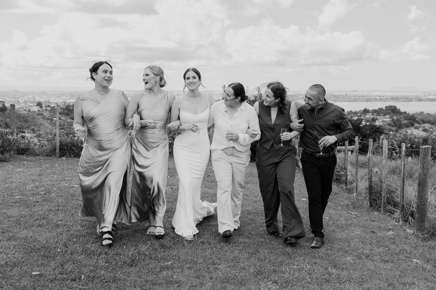A black and white vintage photograph shows a group of people walking arm in arm along a hillside path outdoors.