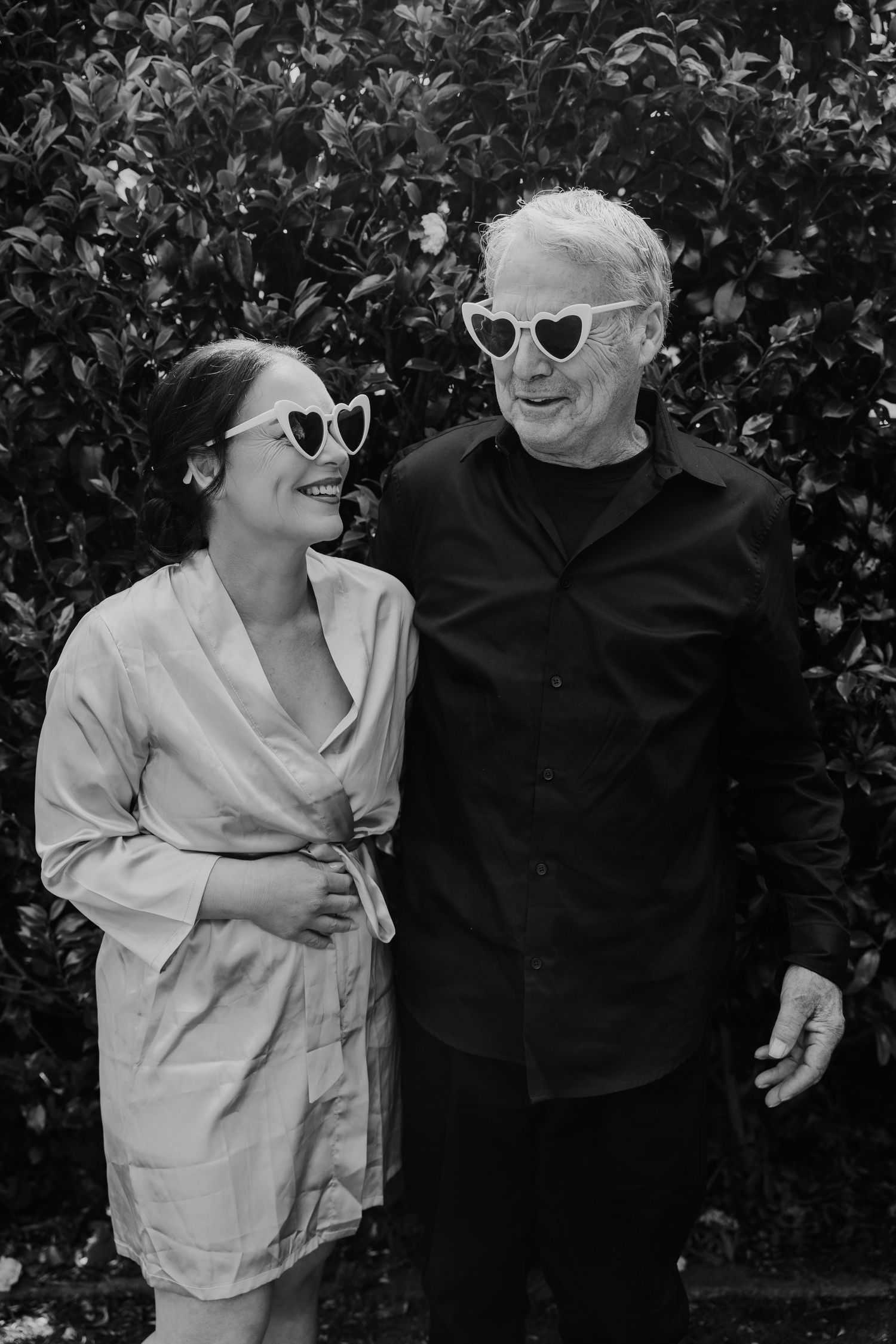 A couple wearing sunglasses poses together in a series of black and white photos against a leafy background.