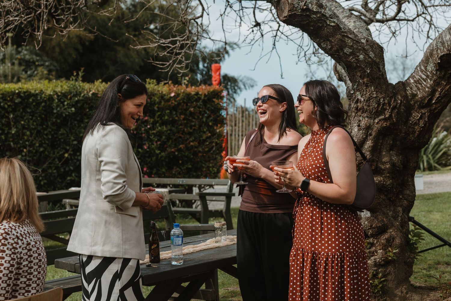 People gathered outdoors for a casual celebration, sharing drinks and conversation in a garden setting.
