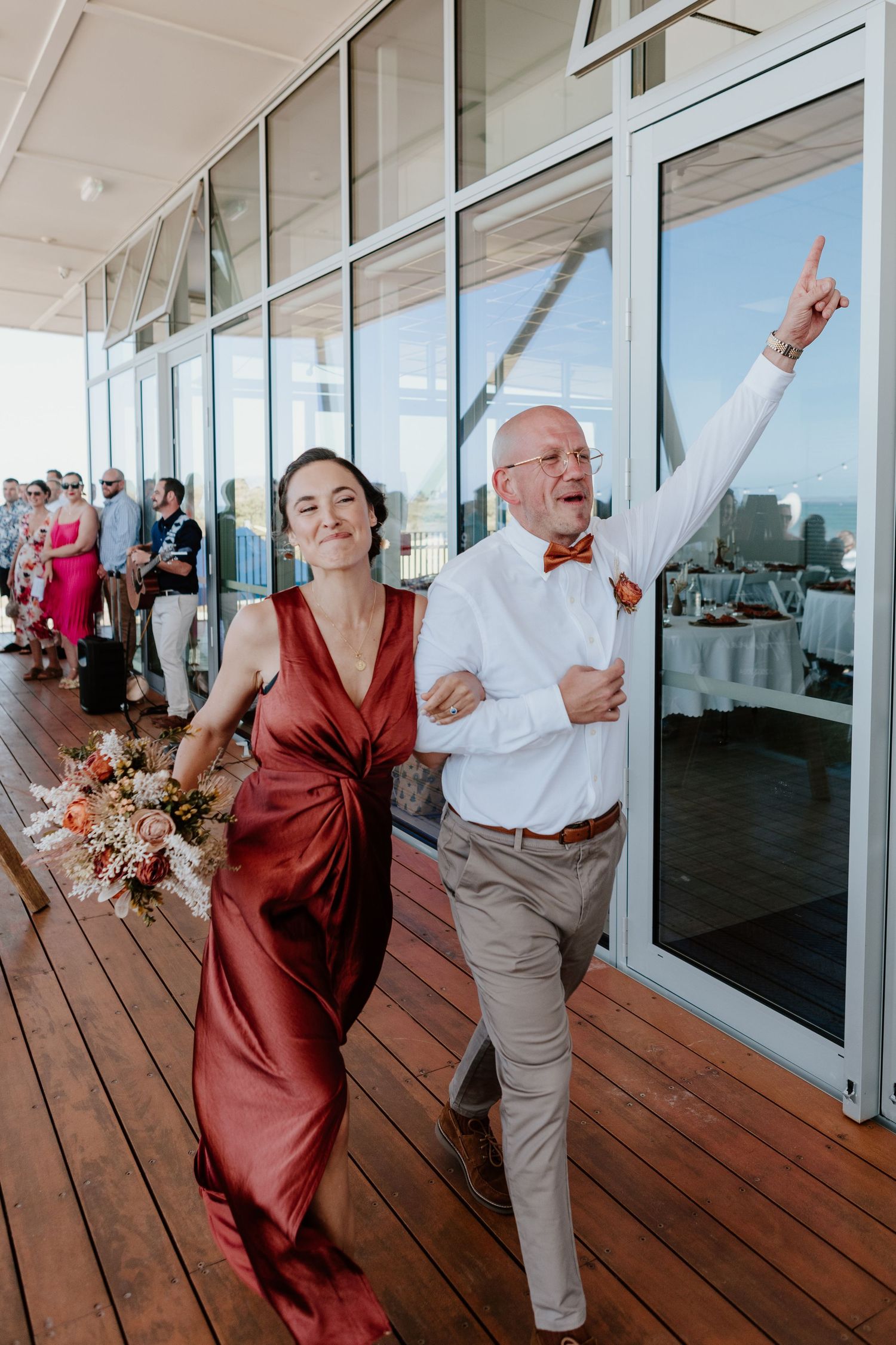 Two attendees celebrate joyfully while walking down a wooden deck at an outdoor event venue with glass windows.
