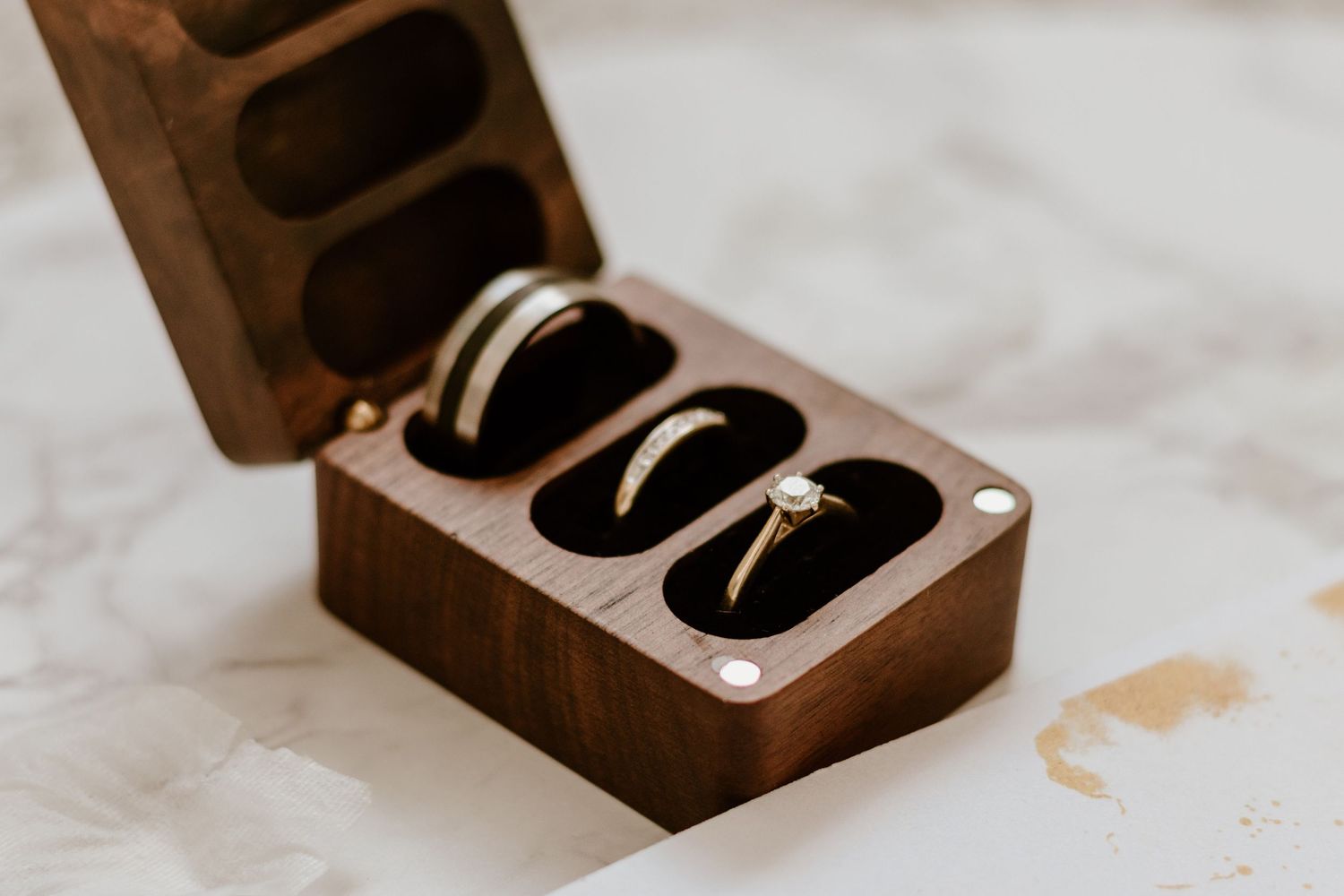 Dark wooden ring box with engagement ring on white marble surface viewed from different angles.