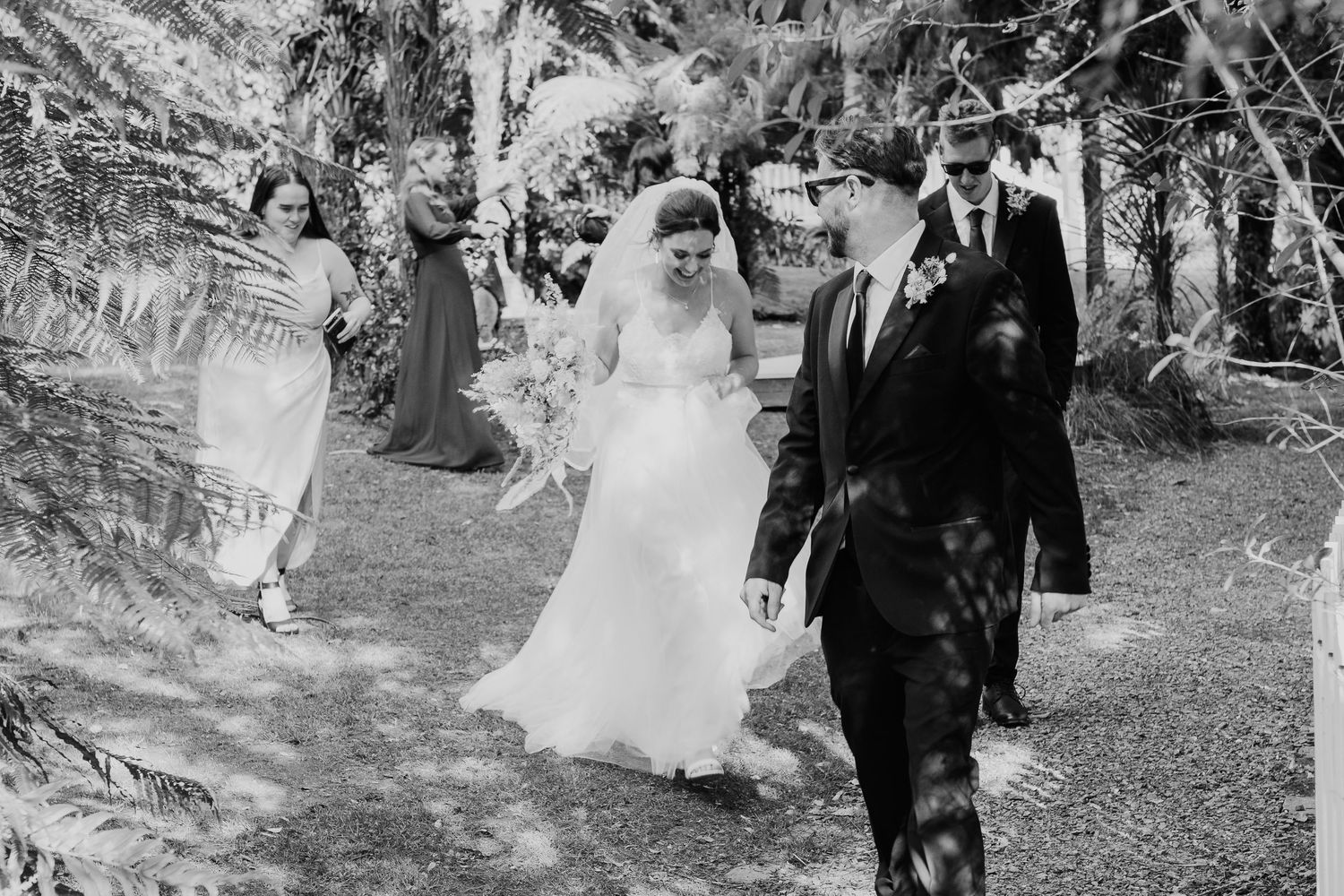 A vintage black and white photograph showing a wedding procession walking along a wooded outdoor path.