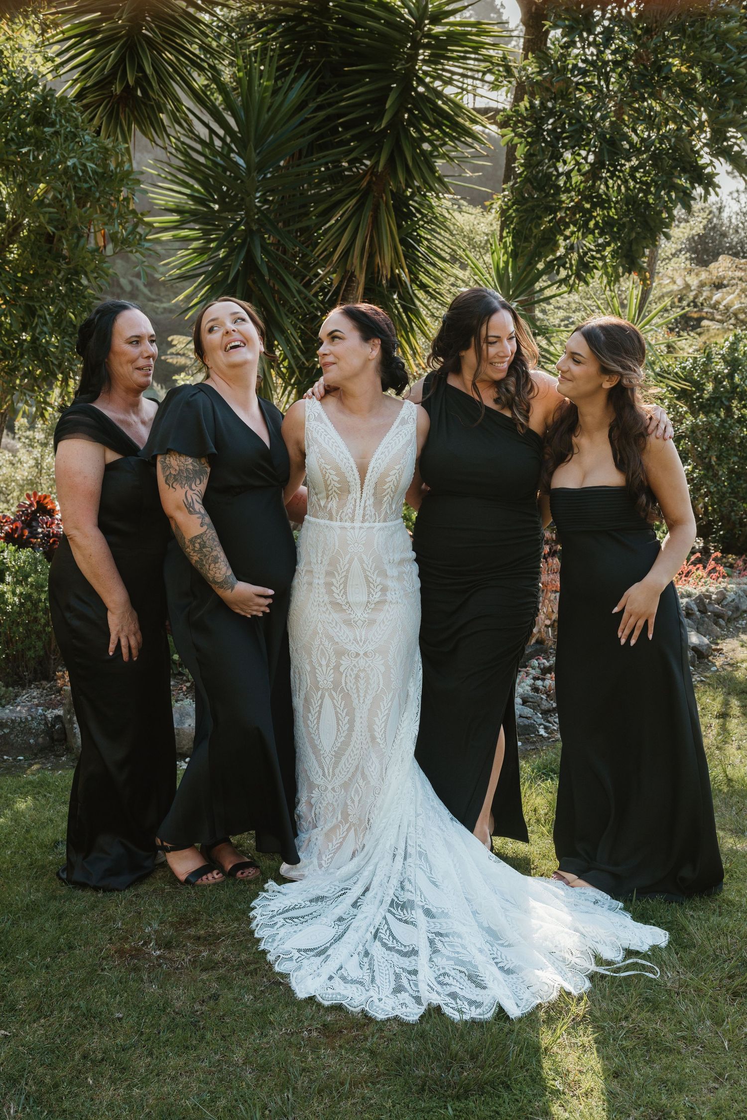 Wedding party wearing black dresses and a white lace gown pose together on grass in a candid photo series.