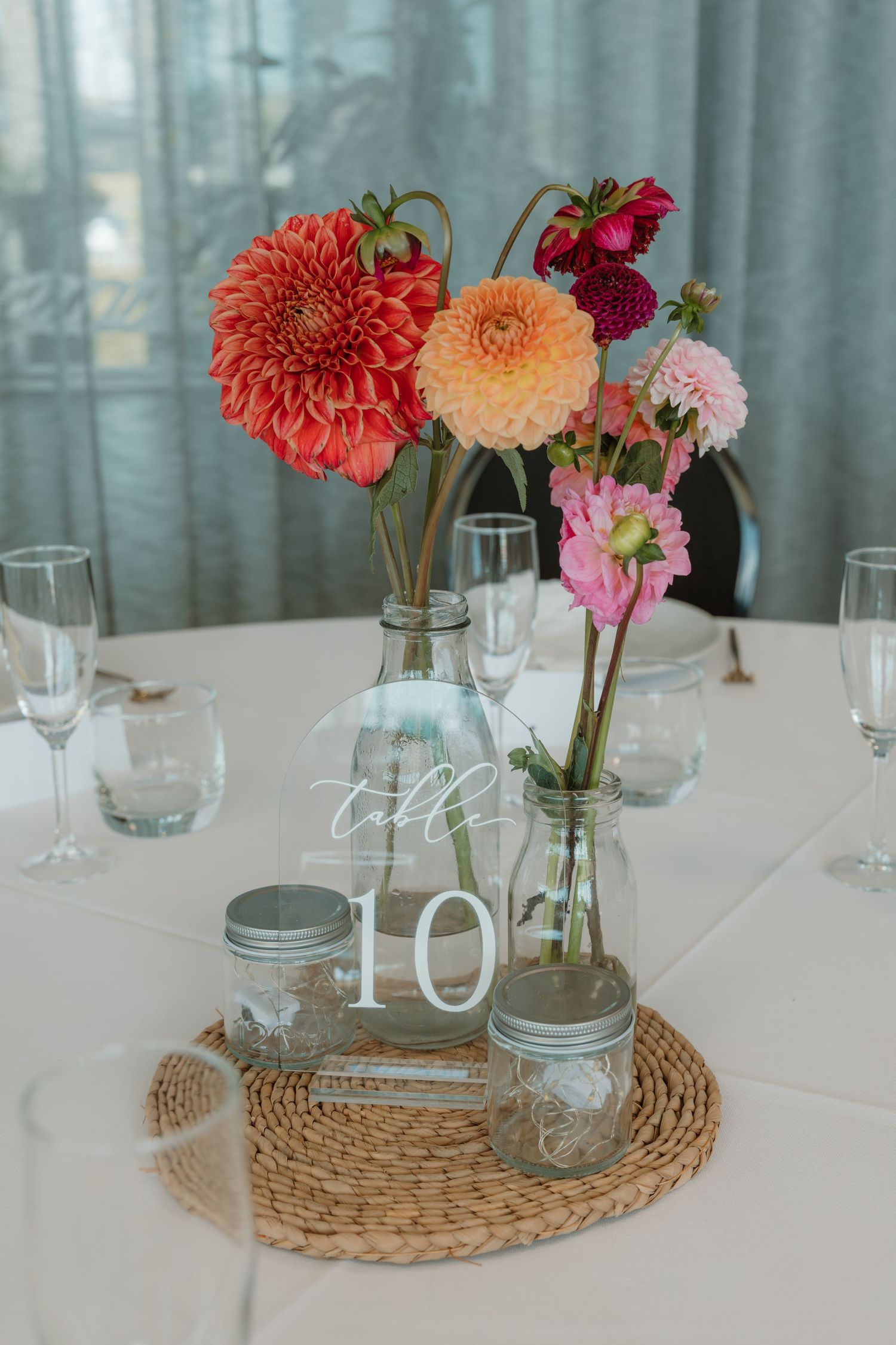 Wedding table centerpiece with colorful dahlias in glass vases on wicker mat with table number 10 sign.