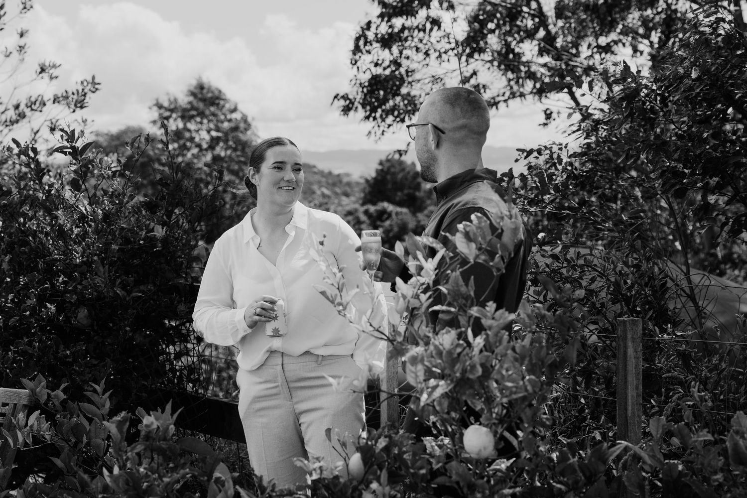 Couple conversing among lush garden greenery in a black and white outdoor photo.