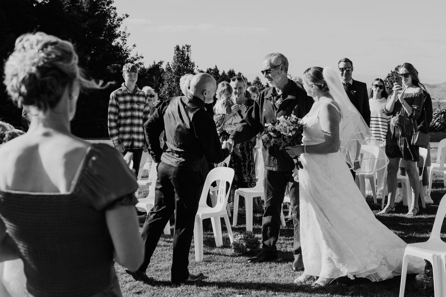 Black and white photo of an outdoor wedding ceremony with guests gathered around in chairs on a lawn.