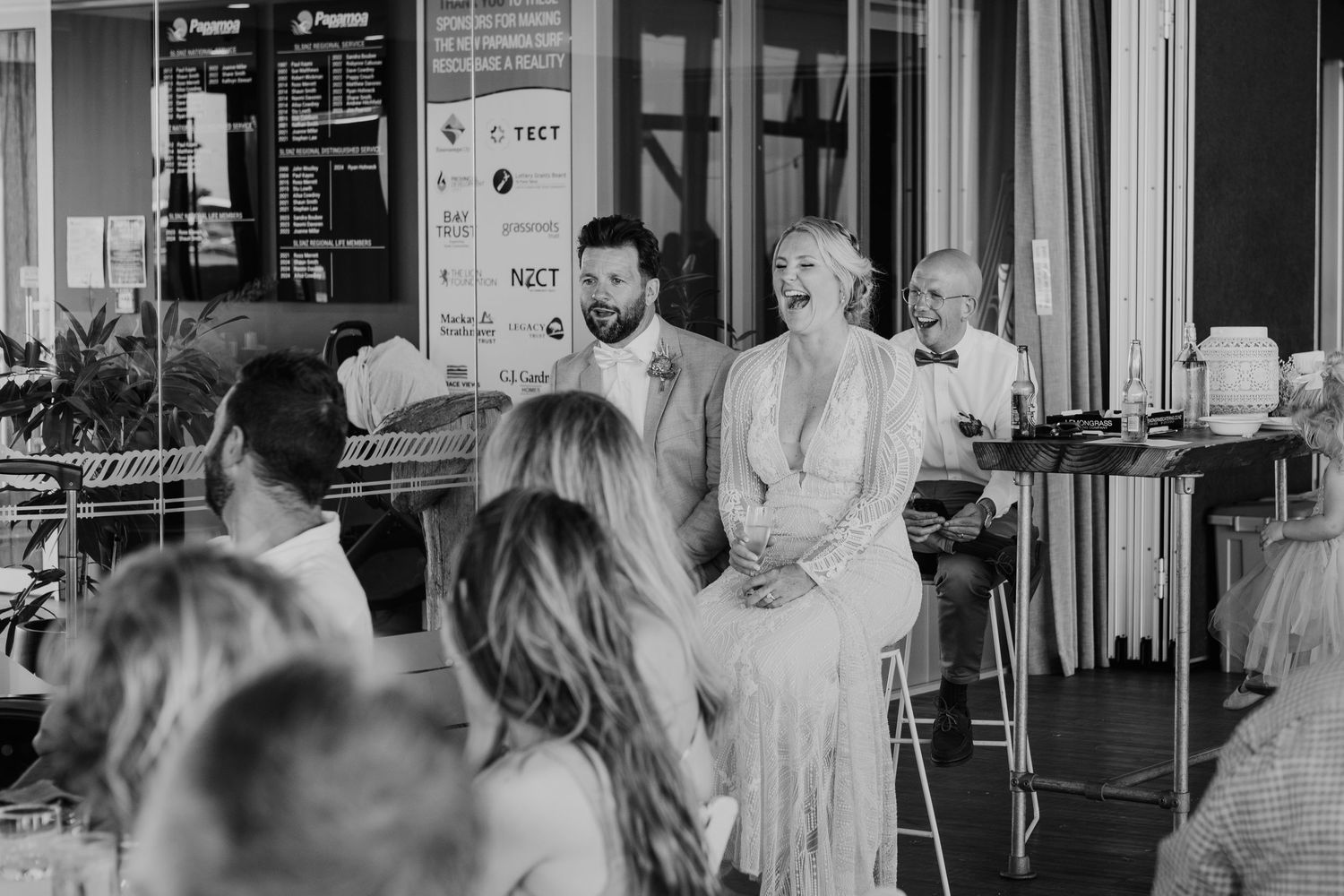 Black and white photo of guests gathered at a restaurant or bar venue with seating along a window.
