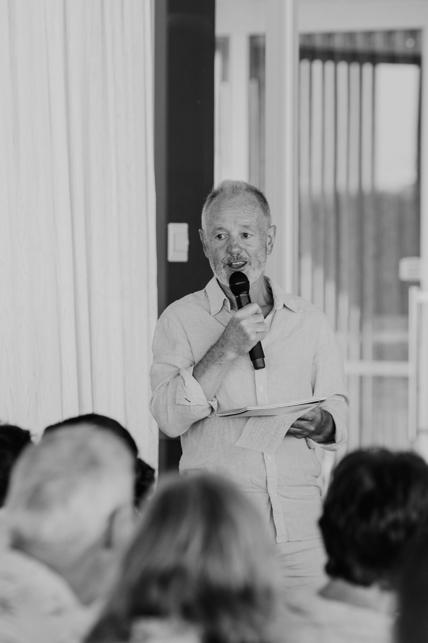 A speaker addresses seated guests at an indoor wedding reception. Father of Groom speech Wedding. Papamoa Surf Lifesaving Club Wedding