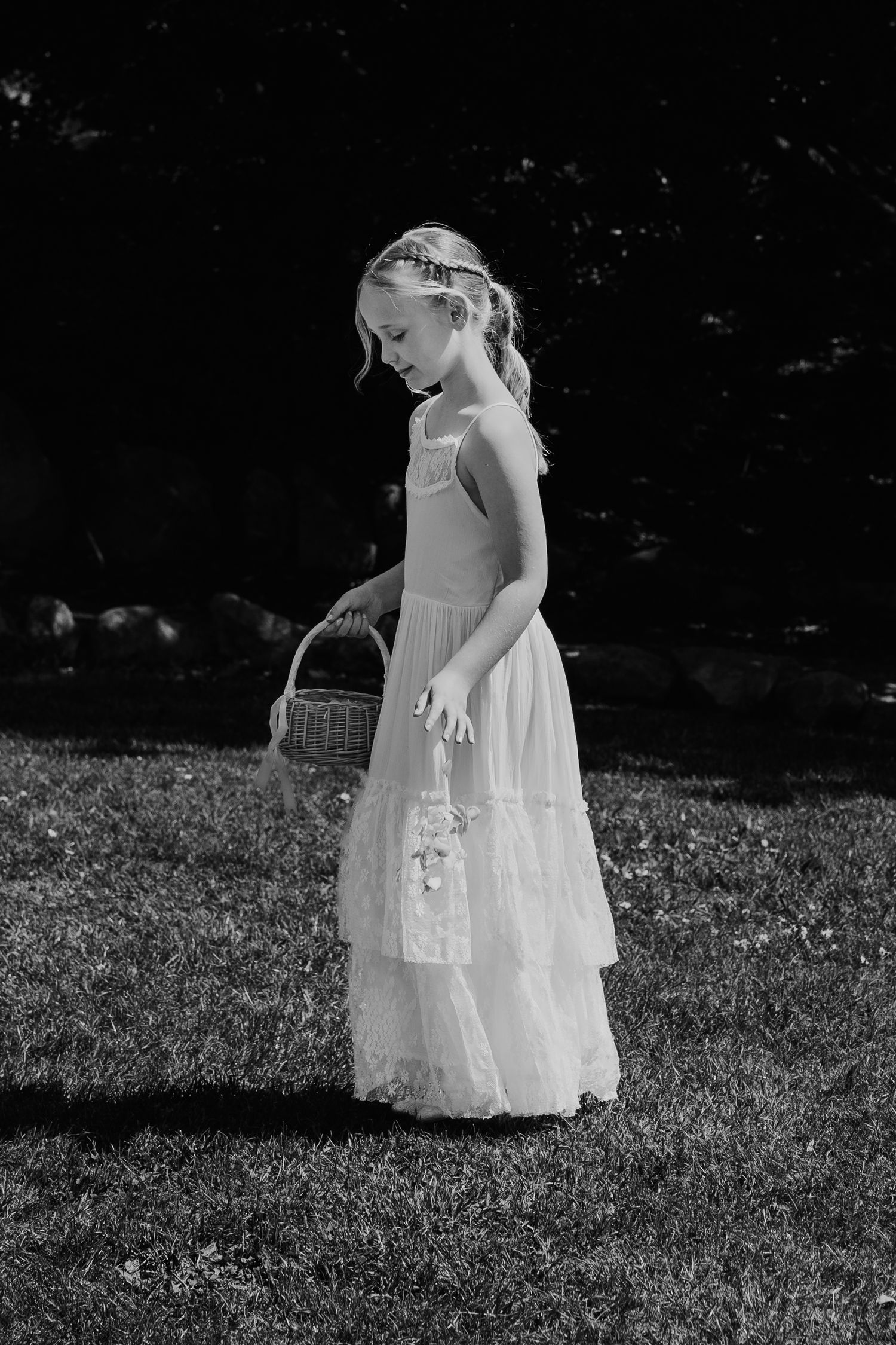 A child in a white dress explores a grassy meadow on a sunny day, captured in black and white photography.