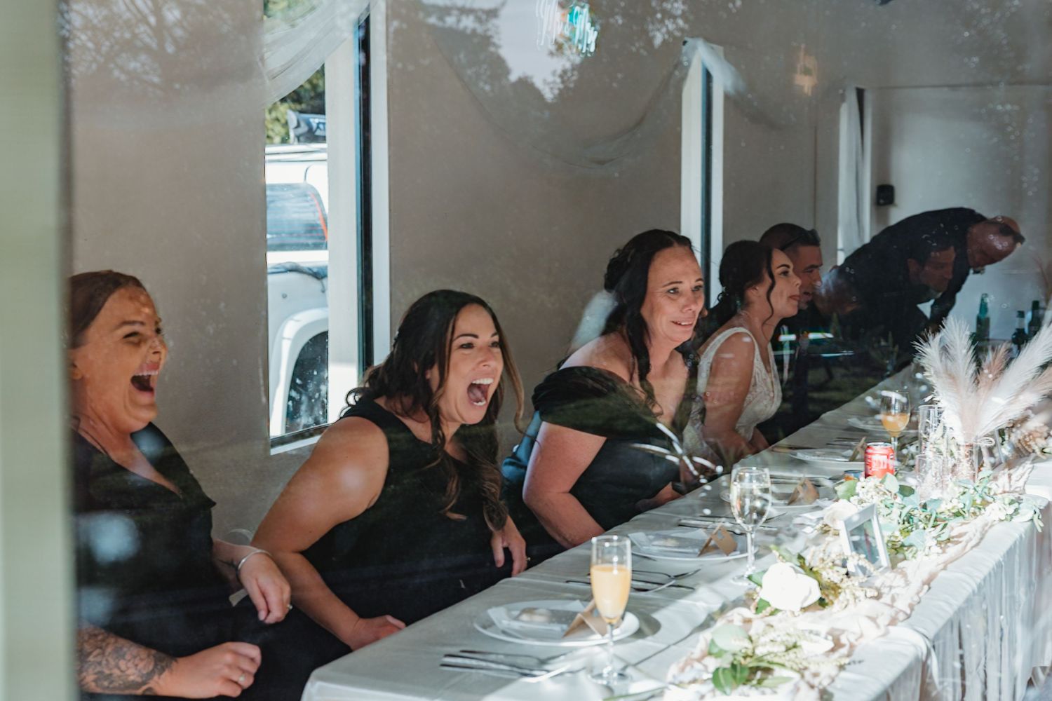 Guests seated at a long white dining table with elegant place settings and candles creating an intimate atmosphere.