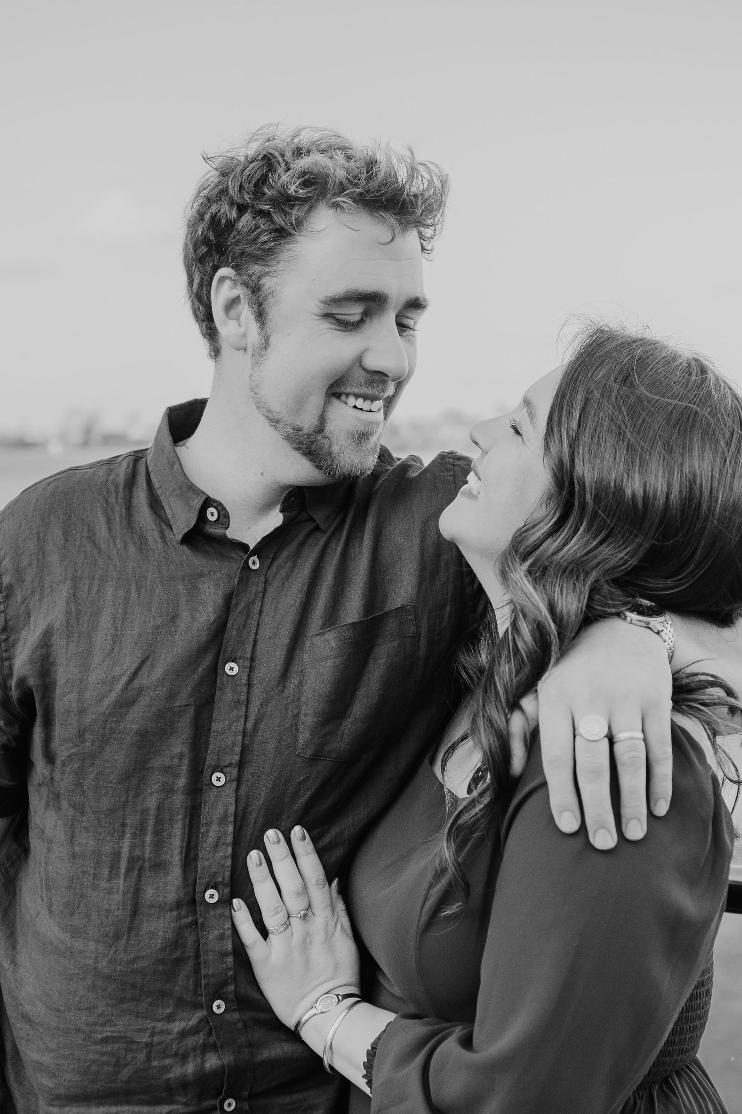 A romantic black and white portrait of a joyful couple embracing and laughing together outdoors.