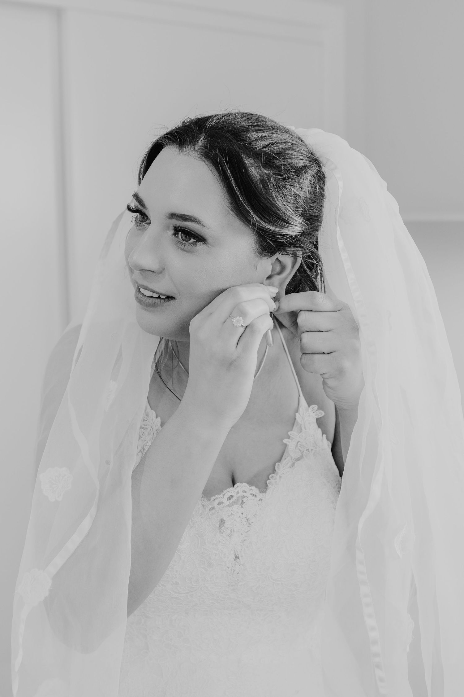 Black and white photo of a bride wearing a lace wedding dress and delicate veil while getting ready.
