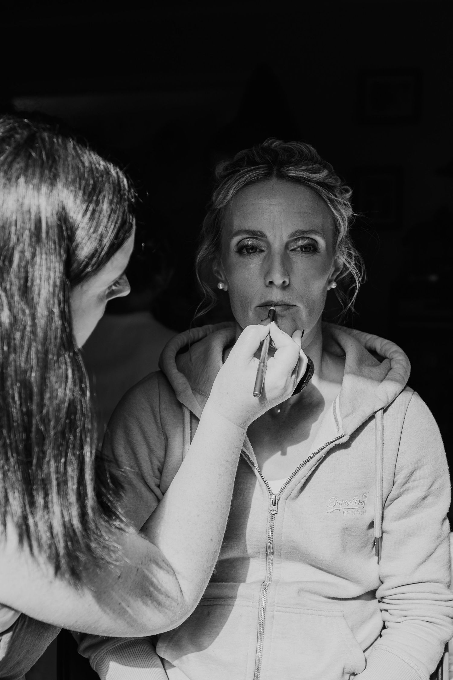 A person applies makeup to a model's face in a dramatic black and white photo.