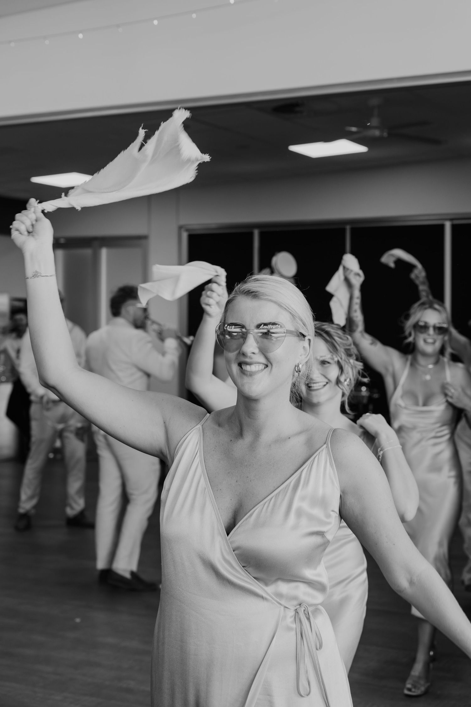 Black and white photo of wedding guests waving napkins on the dance floor during a lively reception celebration.