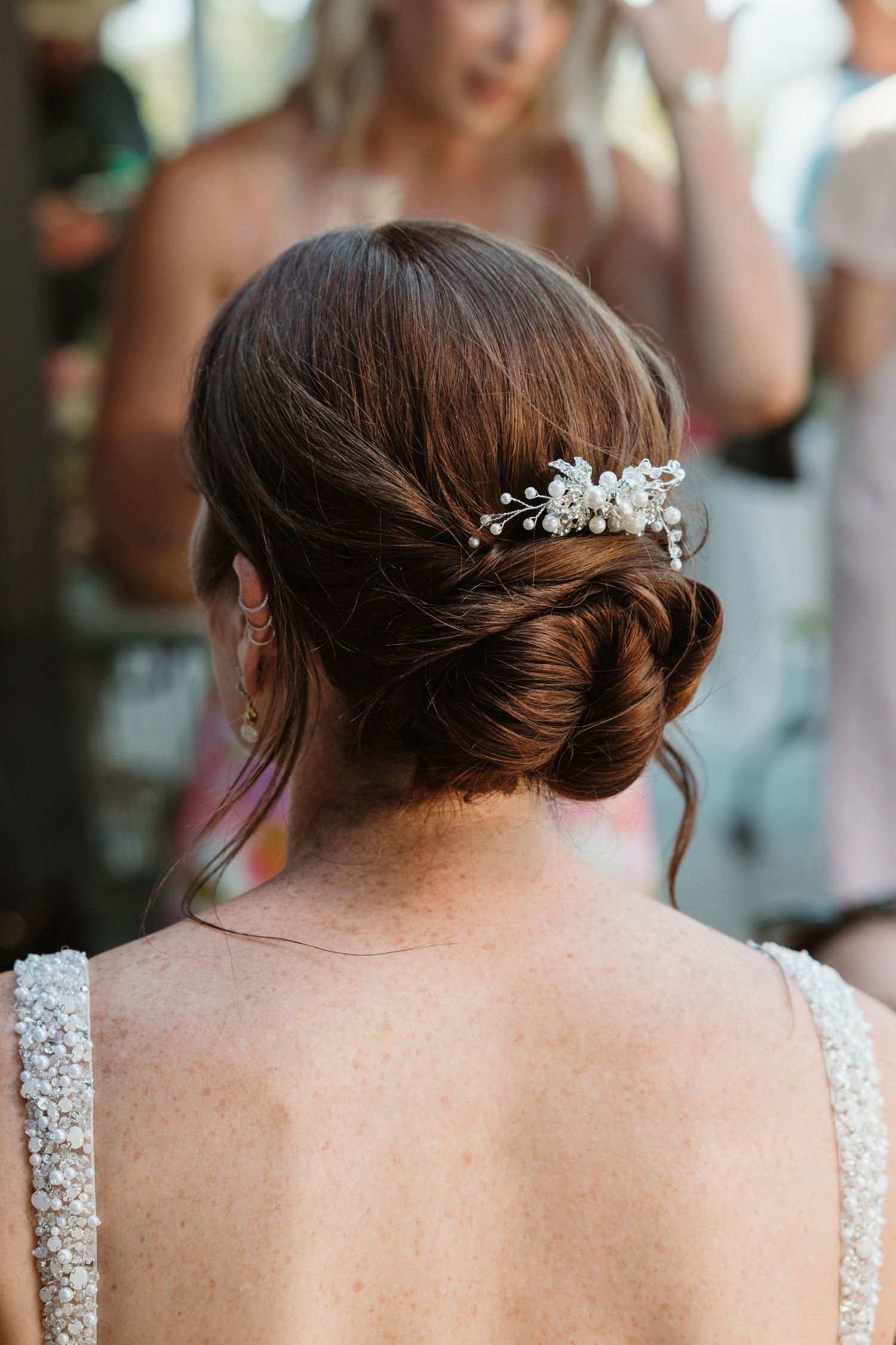 Bride with elegant low chignon updo adorned with delicate floral hair comb, wearing beaded wedding dress.