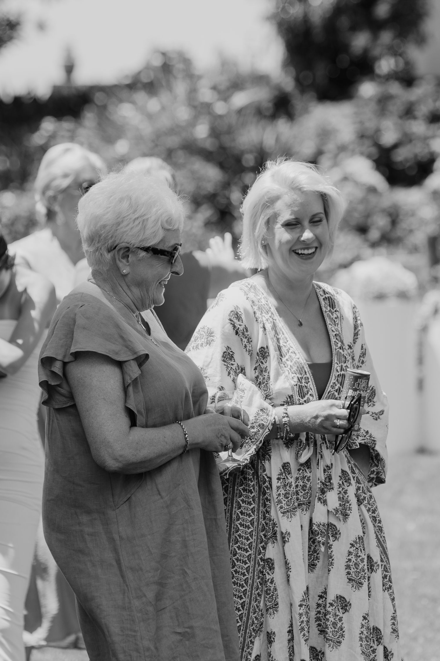 Two women laughing and sharing a moment outdoors at a garden event in black and white photo.
