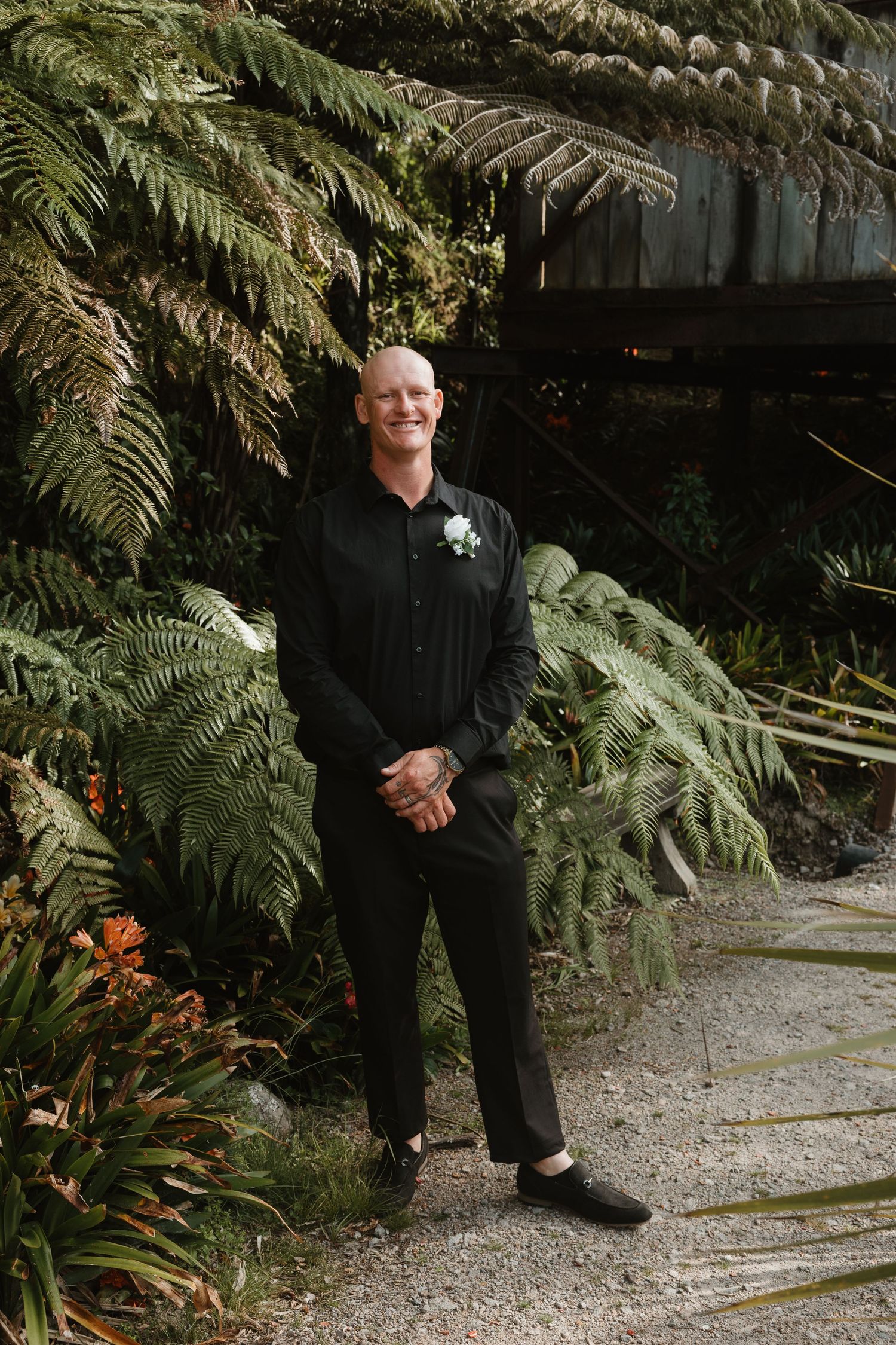 A person stands in a lush garden path surrounded by large ferns and tropical plants in natural lighting.