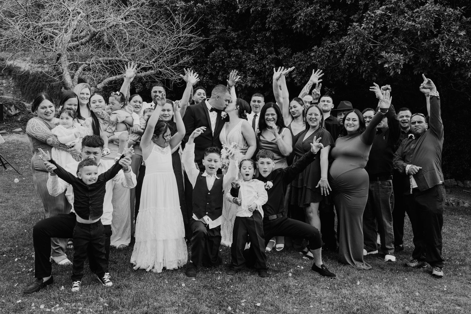 A large wedding party poses together outdoors in a series of black and white group photos.