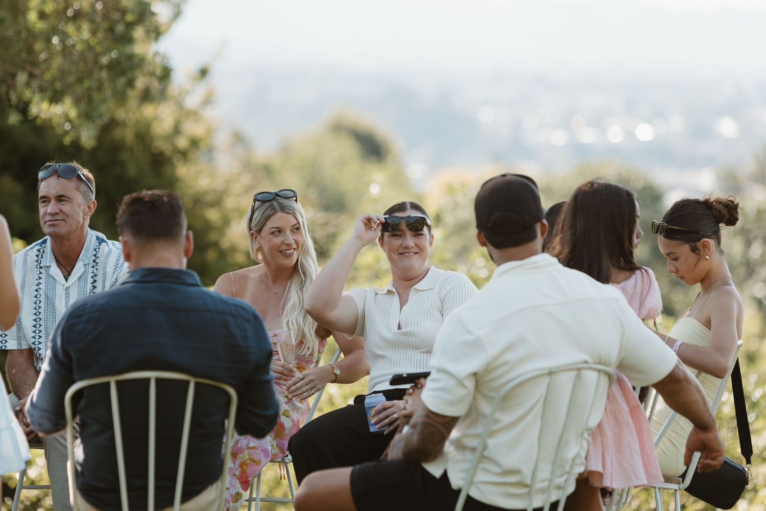 Group of friends enjoying outdoor gathering on a sunny hillside with scenic landscape views in the background.